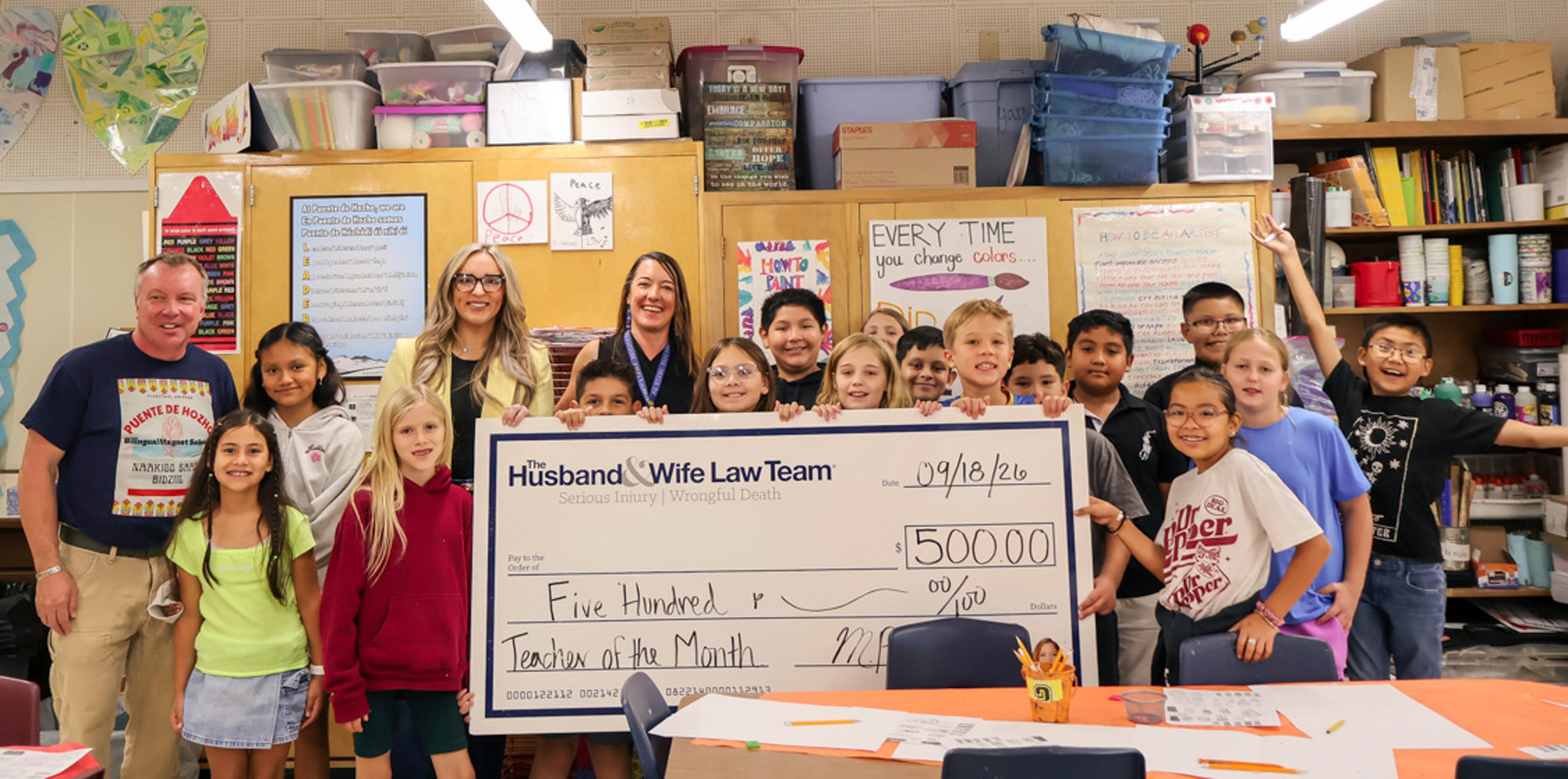 Students and staff gather to celebrate a special Teacher of the Month recognition as a $500 award from the Husband & Wife Law Team is presented in honor of an educator's dedication and positive impact in the classroom.