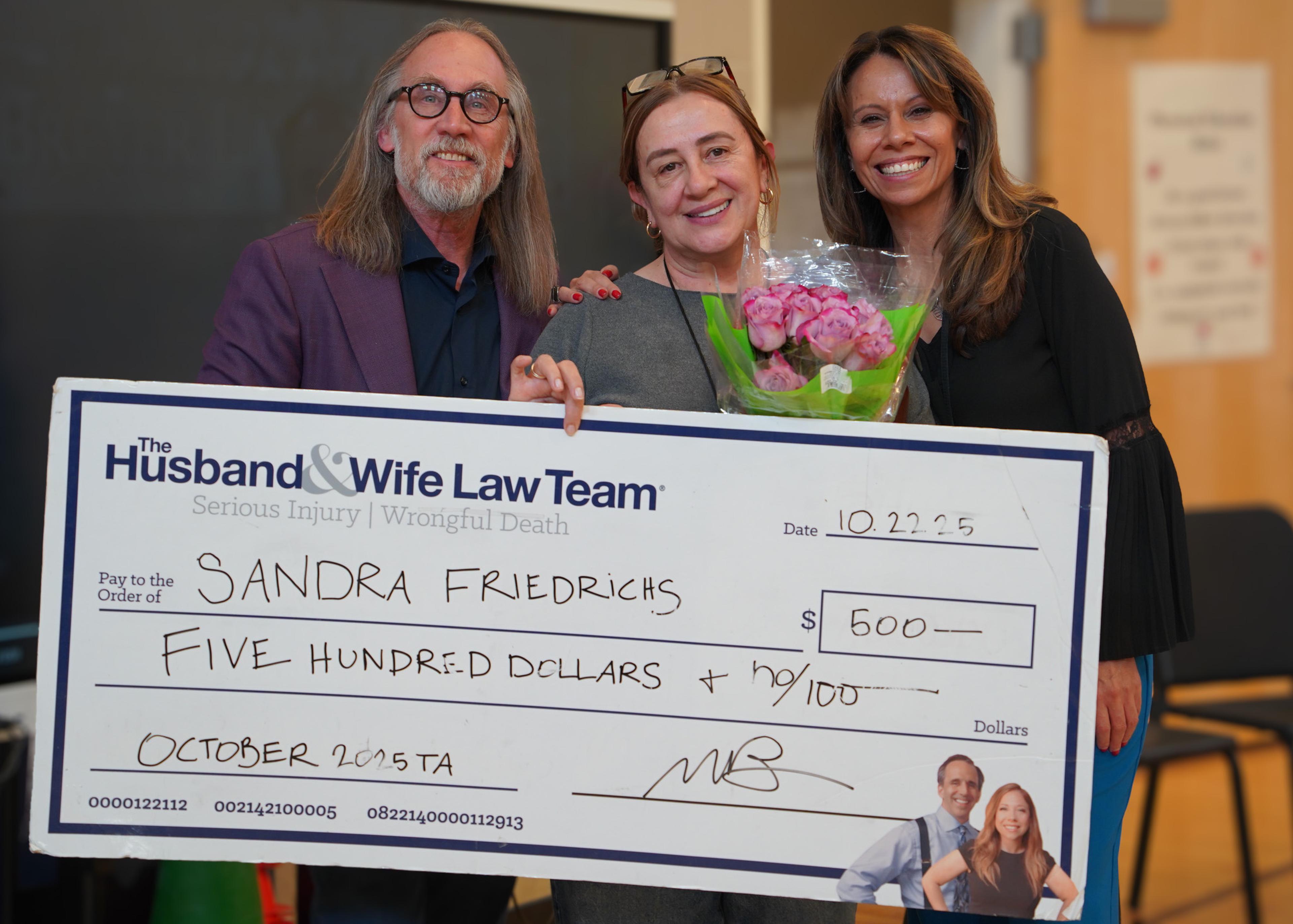 Three smiling people standing with a big check for $500