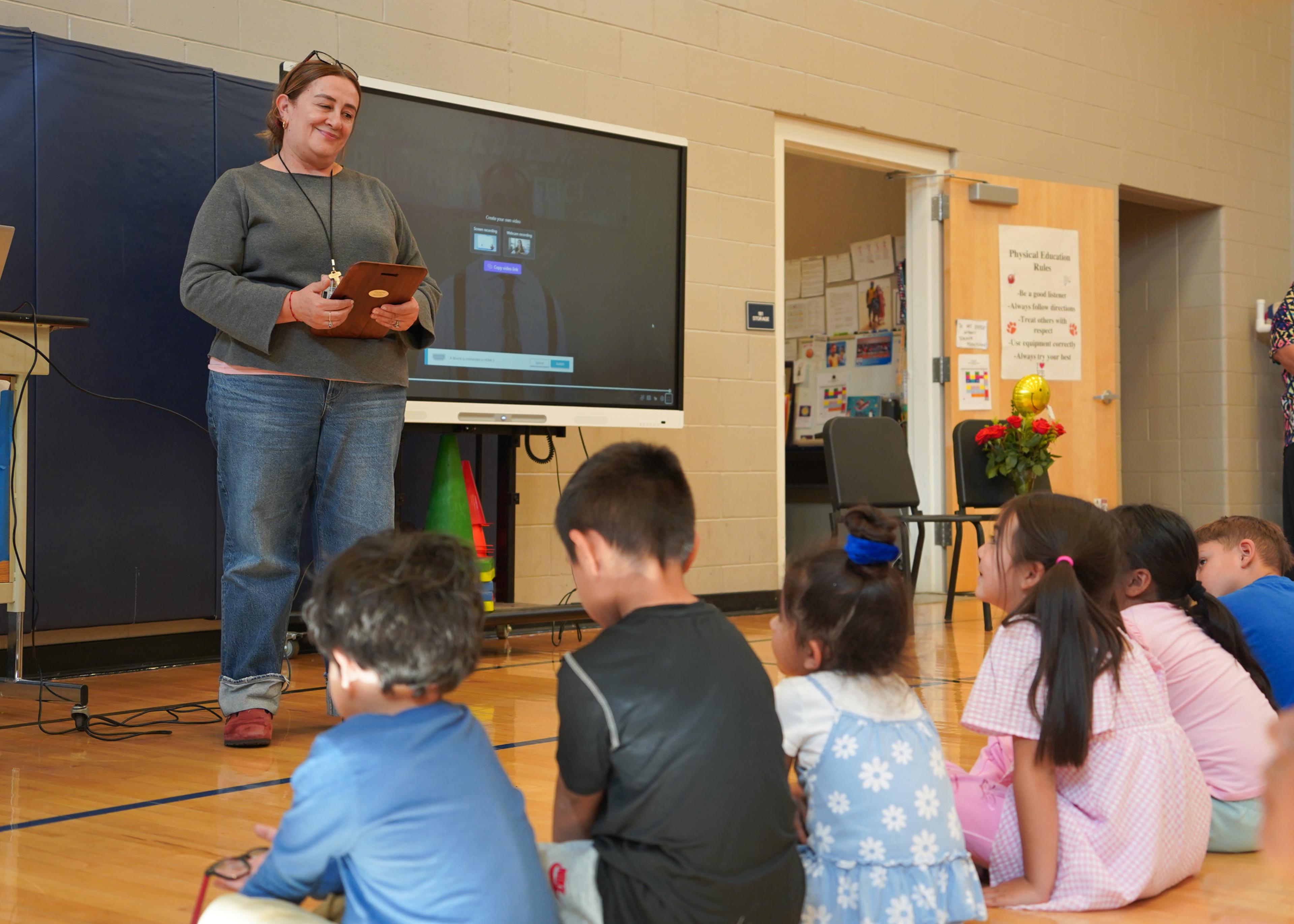 Teacher smiling on her class who is sitting on the floor facing her