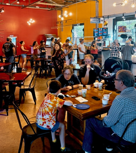 Ice cream like this is hard to find, but these people found it! People at tables and in line in an ice cream shop. Some are ordering and some are eating.