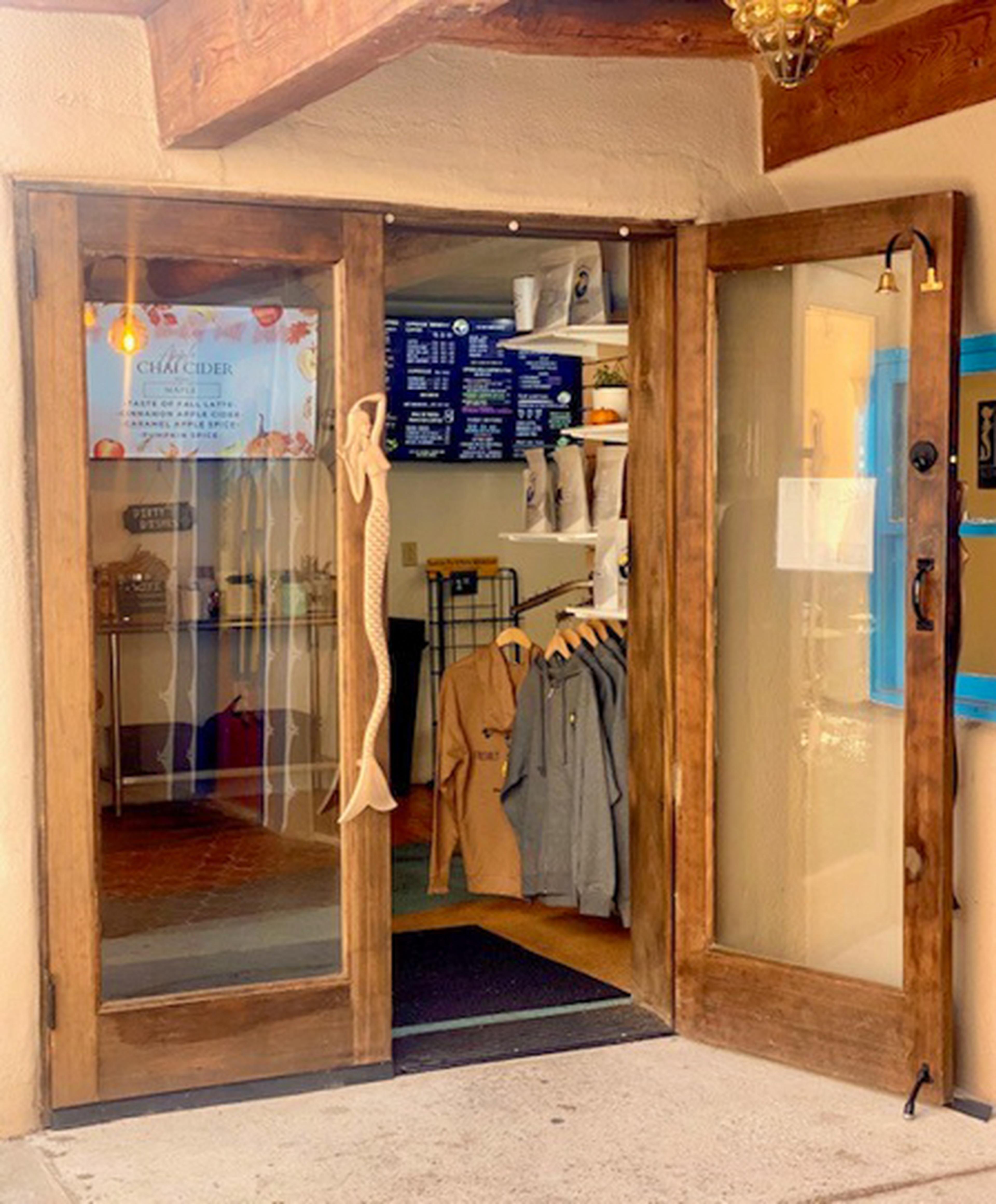 A quaint wooden door opens to a cozy shop interior with hanging jackets, wall menu, and decorative fish handle.