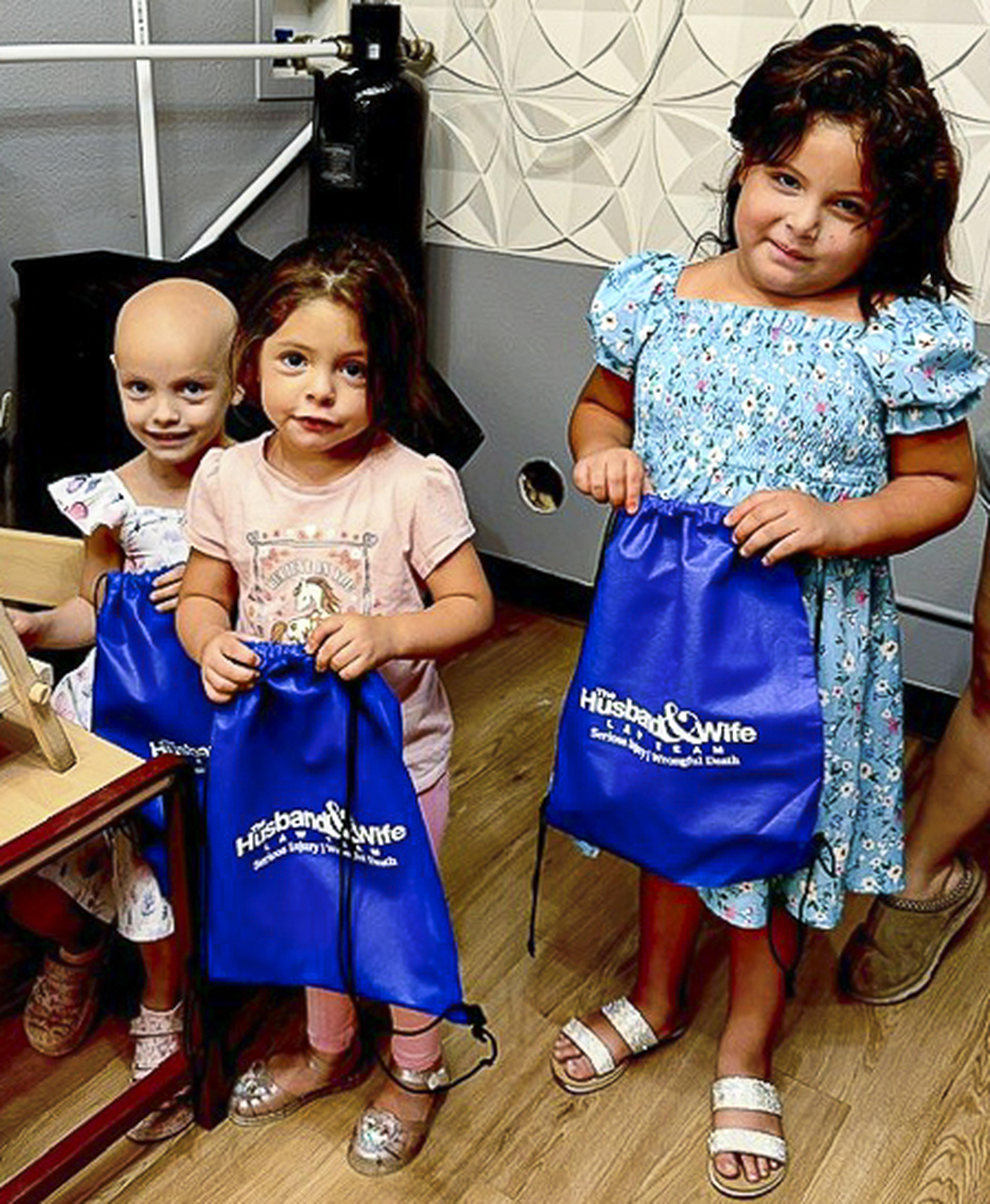 Three smiling children pose with Husband & Wife Law Team gift bags at Route 66 Coffee & Boba Co., celebrating a fun-filled community event.