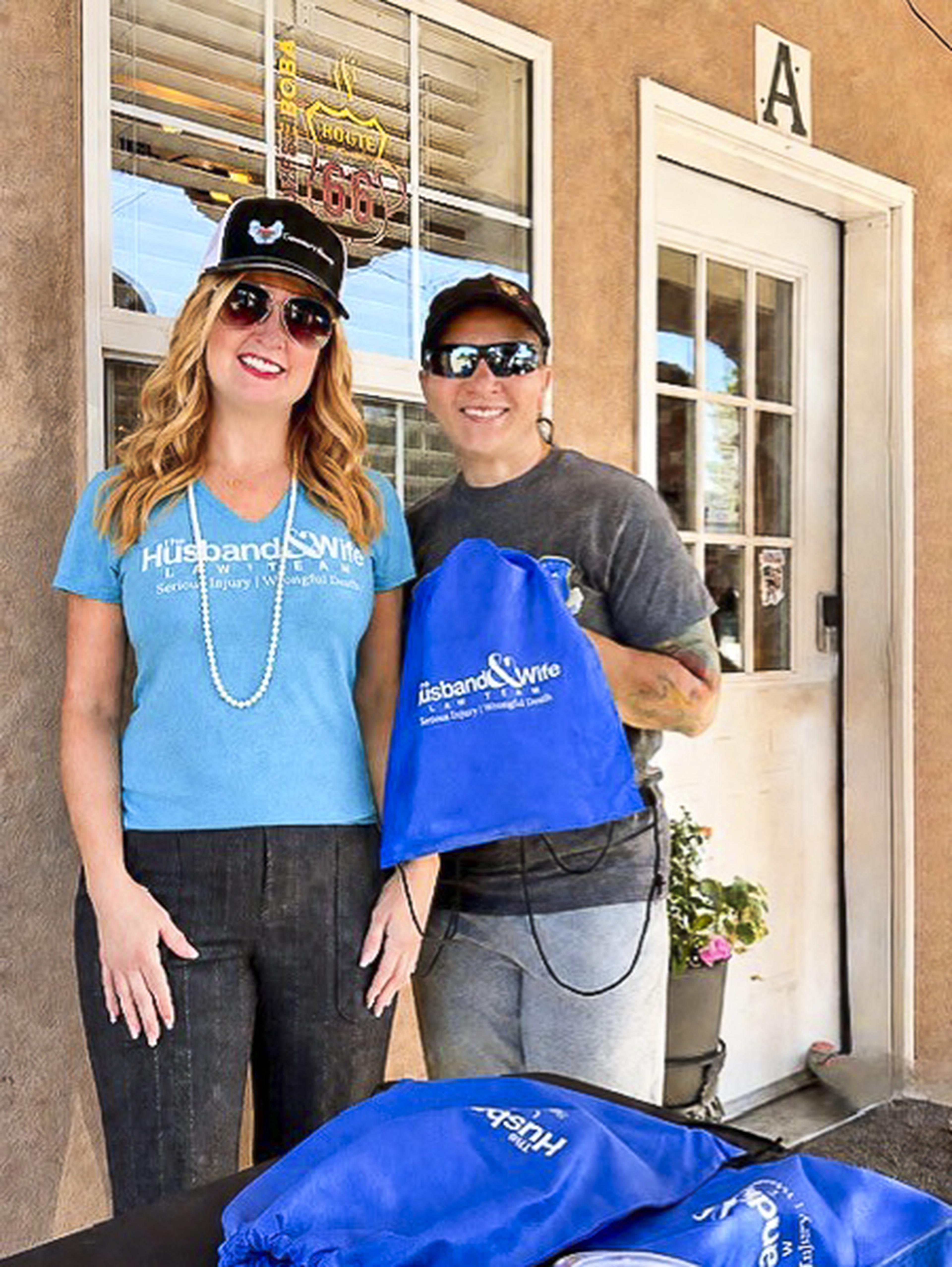 Standing outside Route 66 Coffee & Boba Co., two attendees proudly display their Husband & Wife Law Team gift bag as they enjoy a day of community connection and fun.