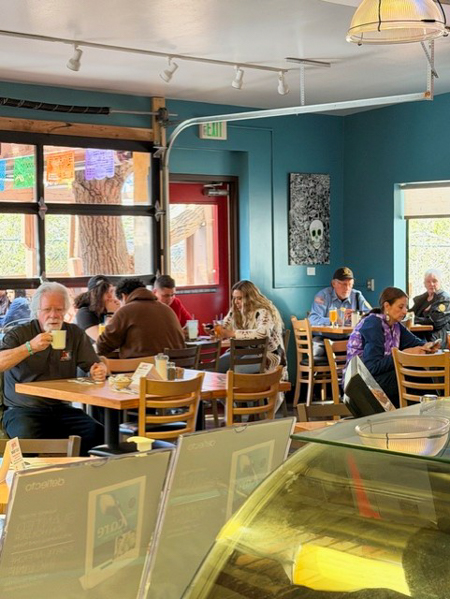 People dine and chat at tables inside Bonita Restaurant, surrounded by colorful banners and a teal wall featuring artwork. People seated at tables inside the Bonita Restaurant, drinking and eating. Decor includes colorful banners and a skull artwork on a teal wall.