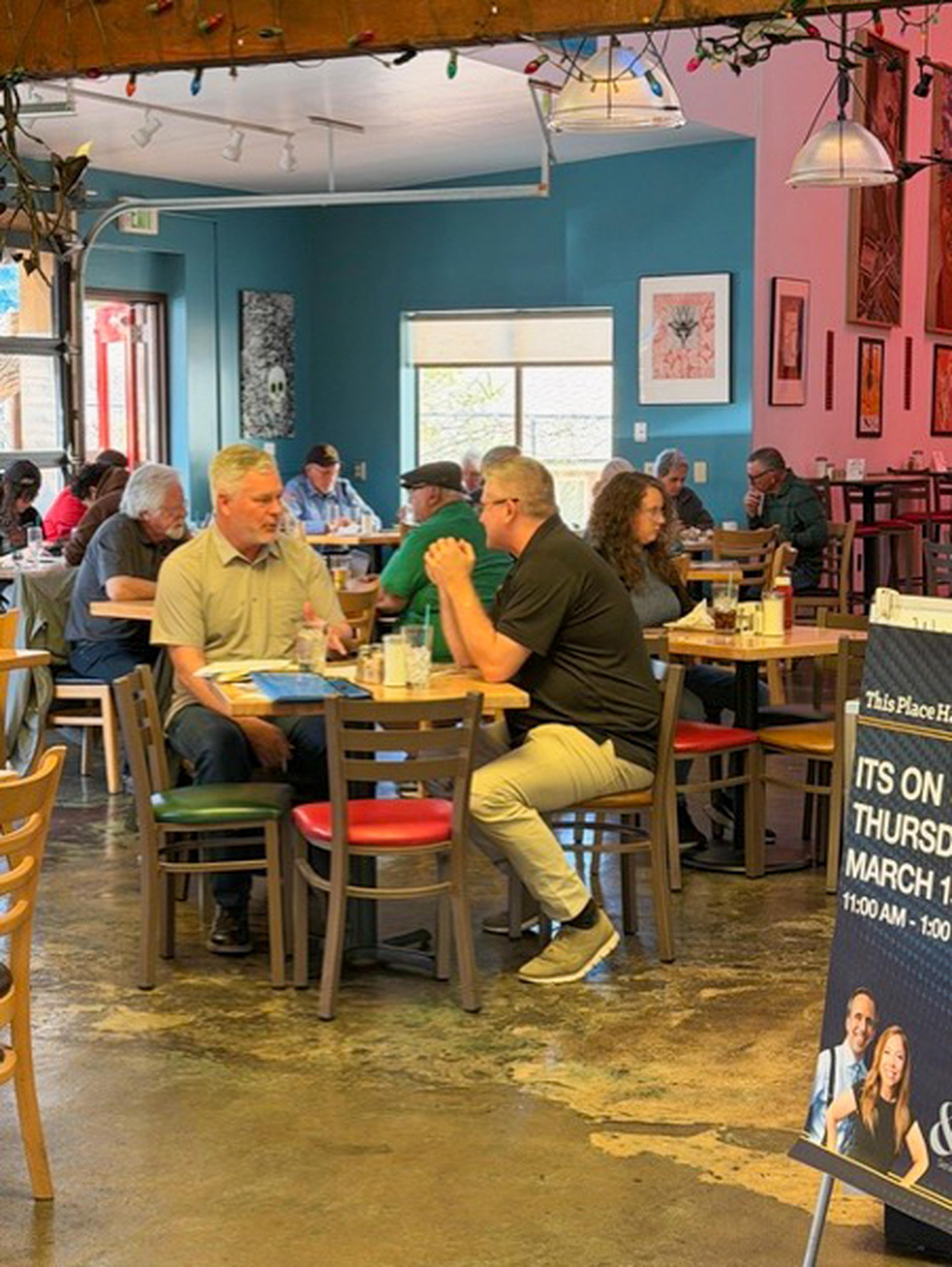 Customers sitting at the Bonita Restaurant tables, engaged in conversation. A signboard with event details is visible in the foreground.