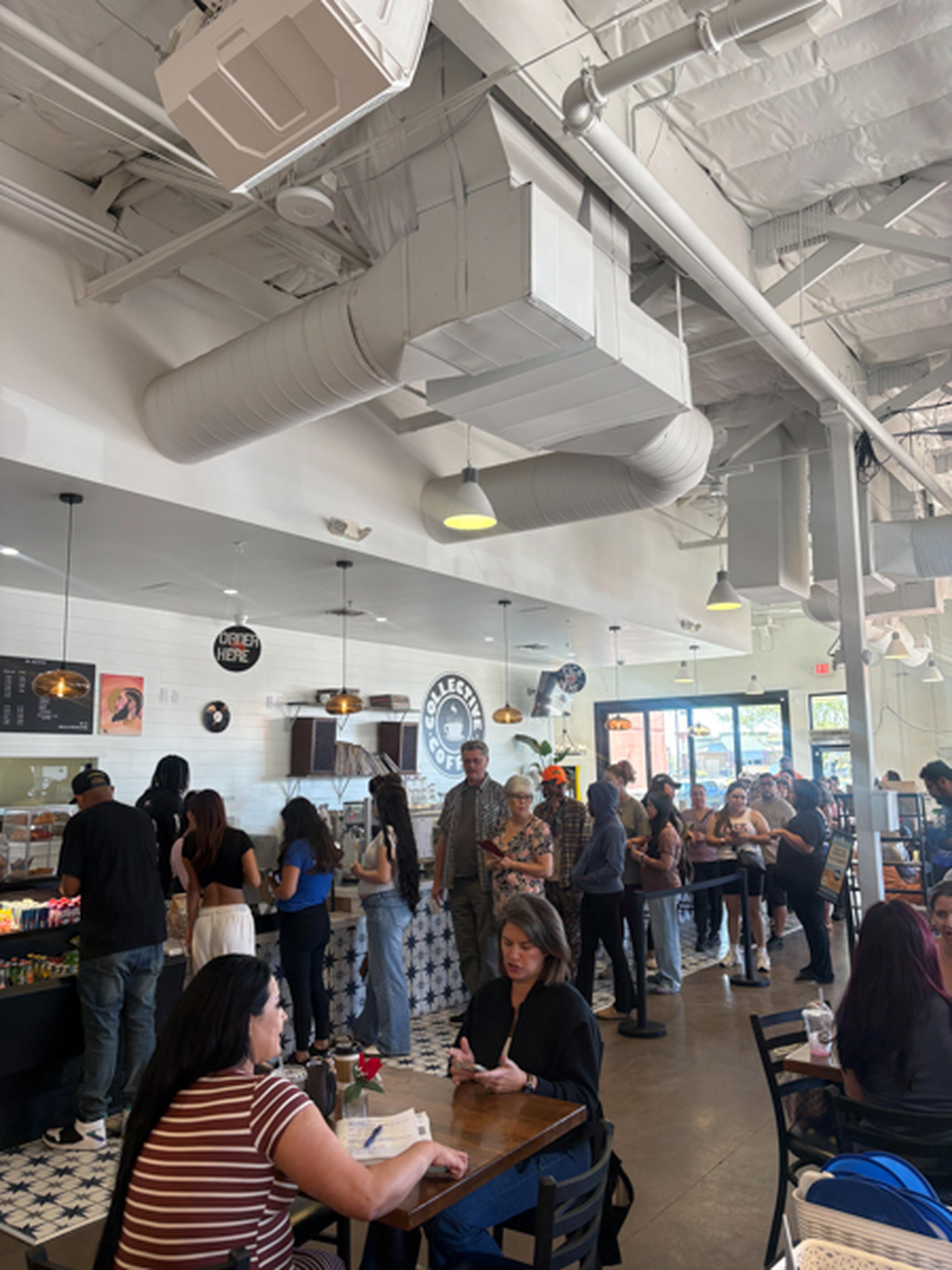 Collective Coffee bustles with energy as people line up at the counter and chat at tables beneath bright lights and exposed ductwork.