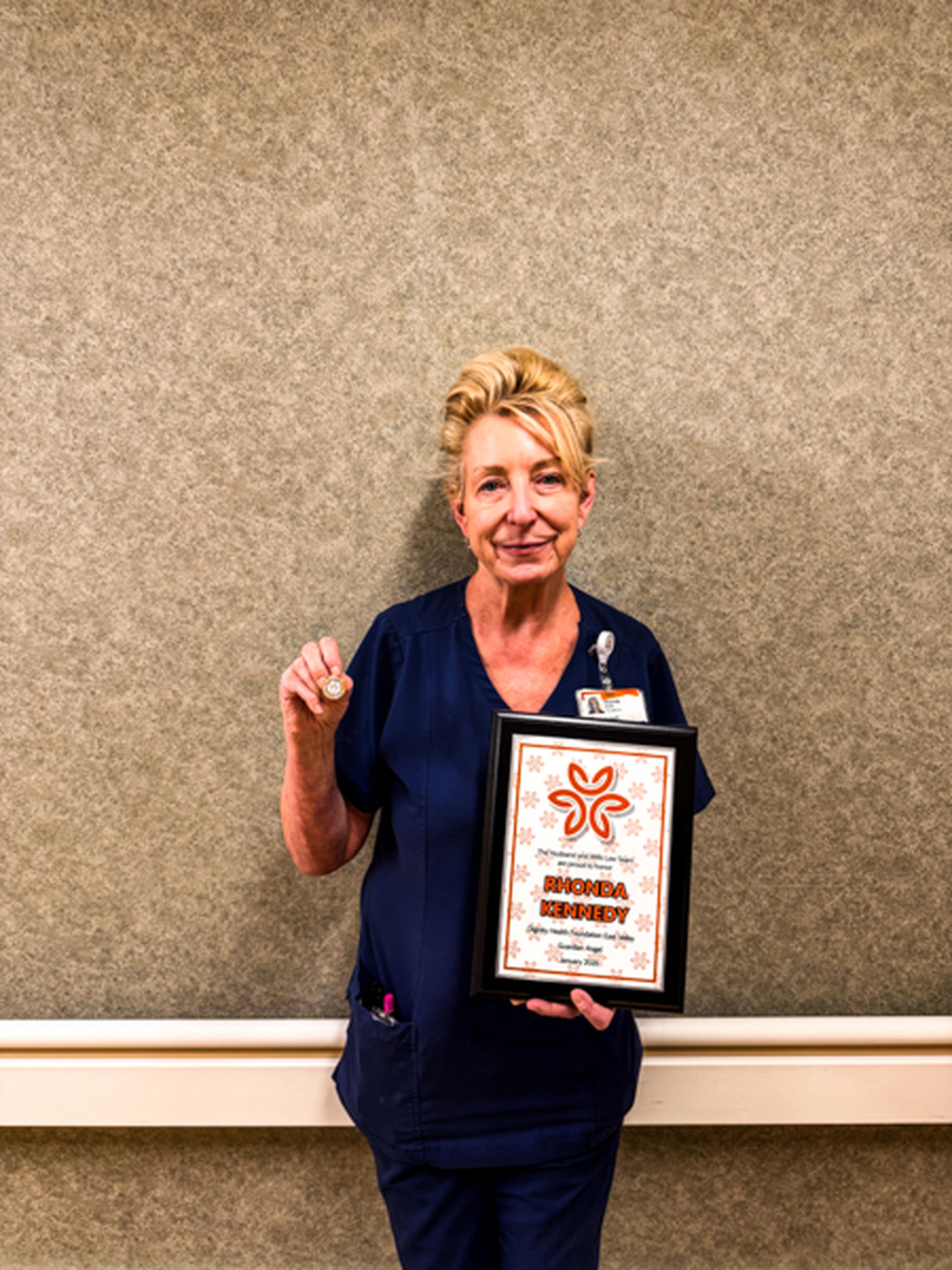 Nurse Rhonda holds a framed Guardian Angel Award from the Husband & Wife Law Team