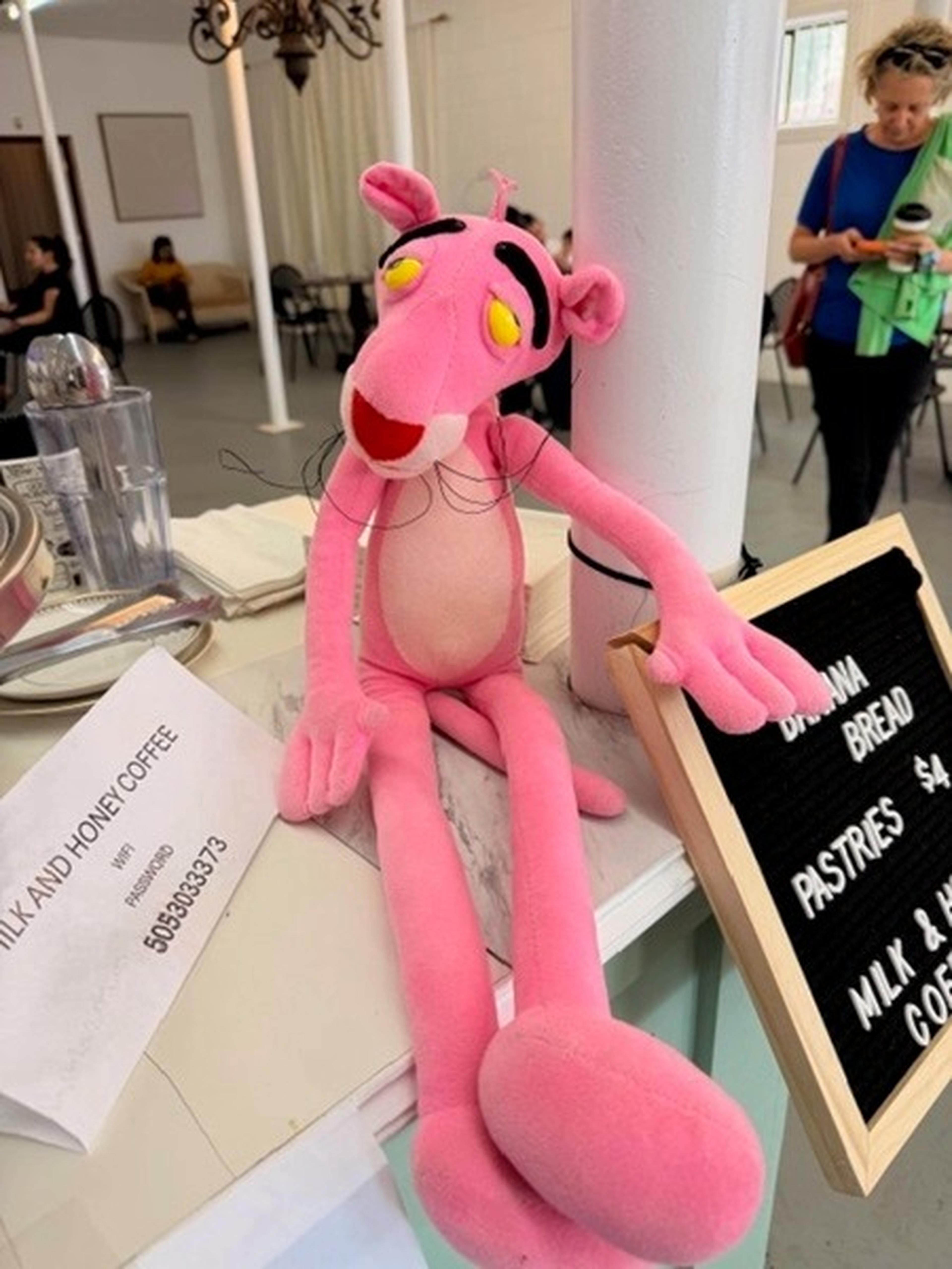 A Pink Panther plush sits playfully on the countertop beside the menu board at Milk and Honey Caffe