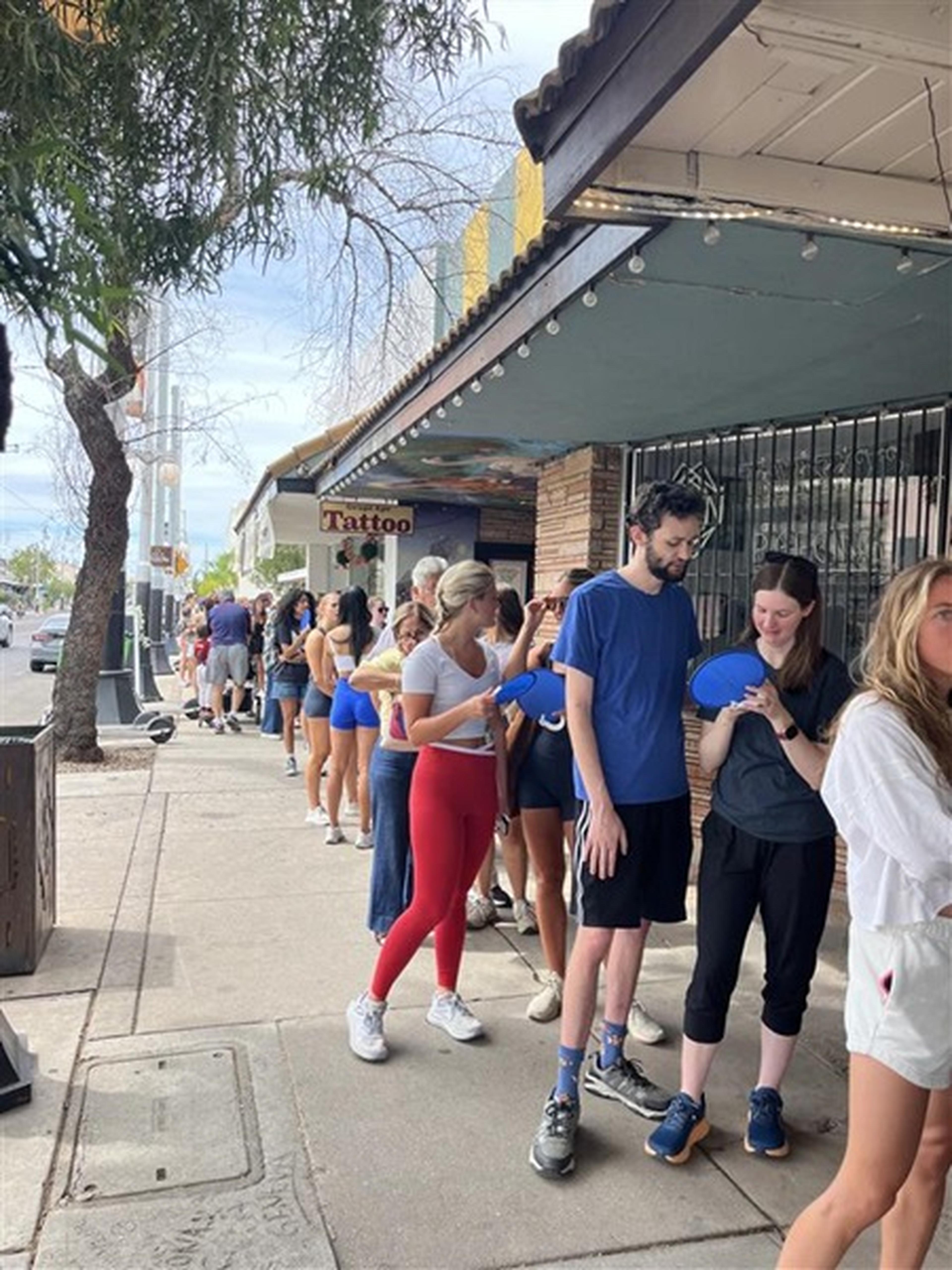 Hungry customers line up outside the 1989 Bakehouse under a green awning, holding blue Husband & Wife Law Team fans.