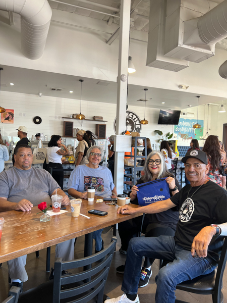 Four friends smile around a wooden table at Collective Coffee, drinks in hand