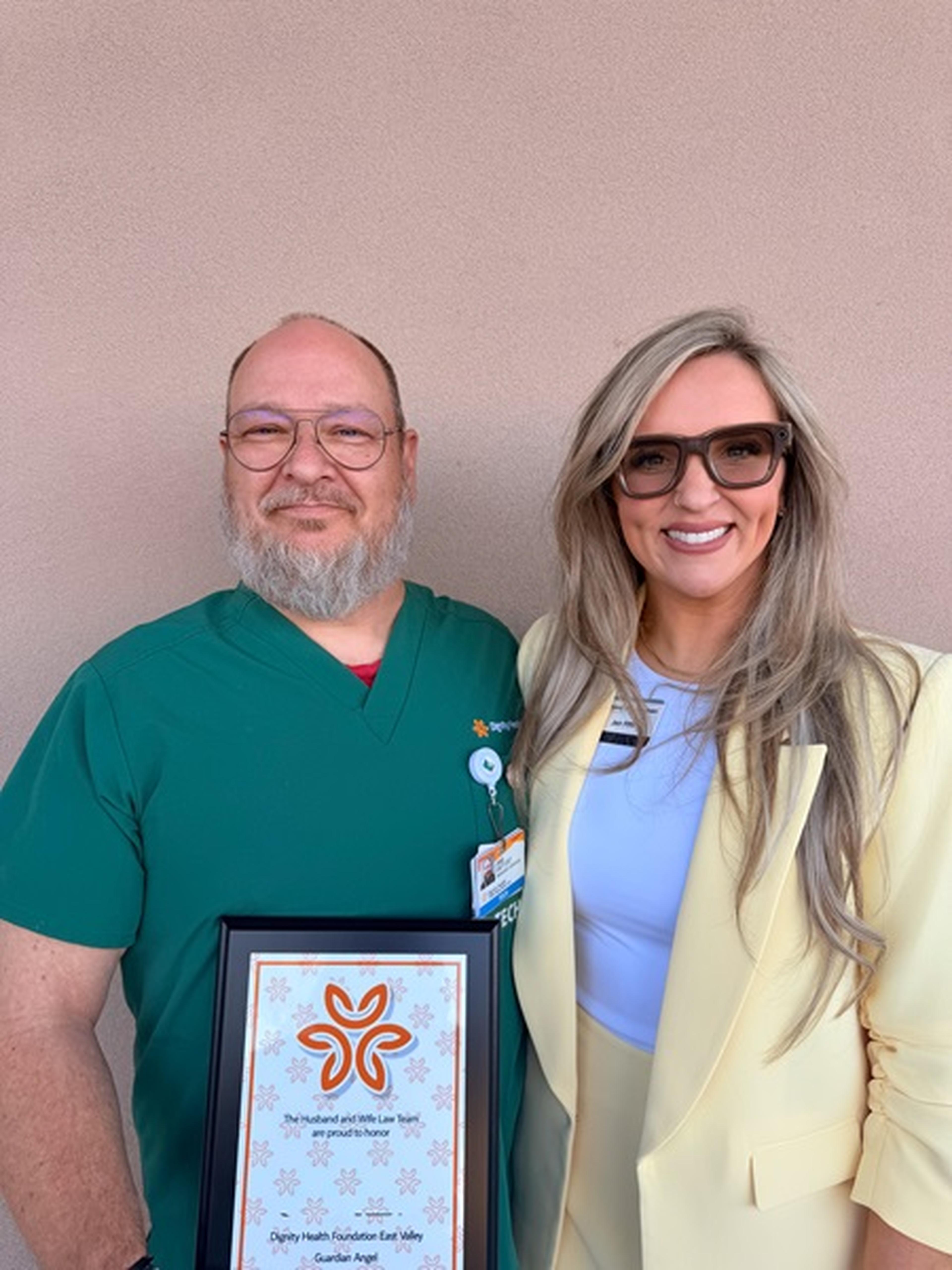 Framed certificate in hand, Jody stands tall next to a Husband & Wife Law Team representative, both sharing a triumphant smile.