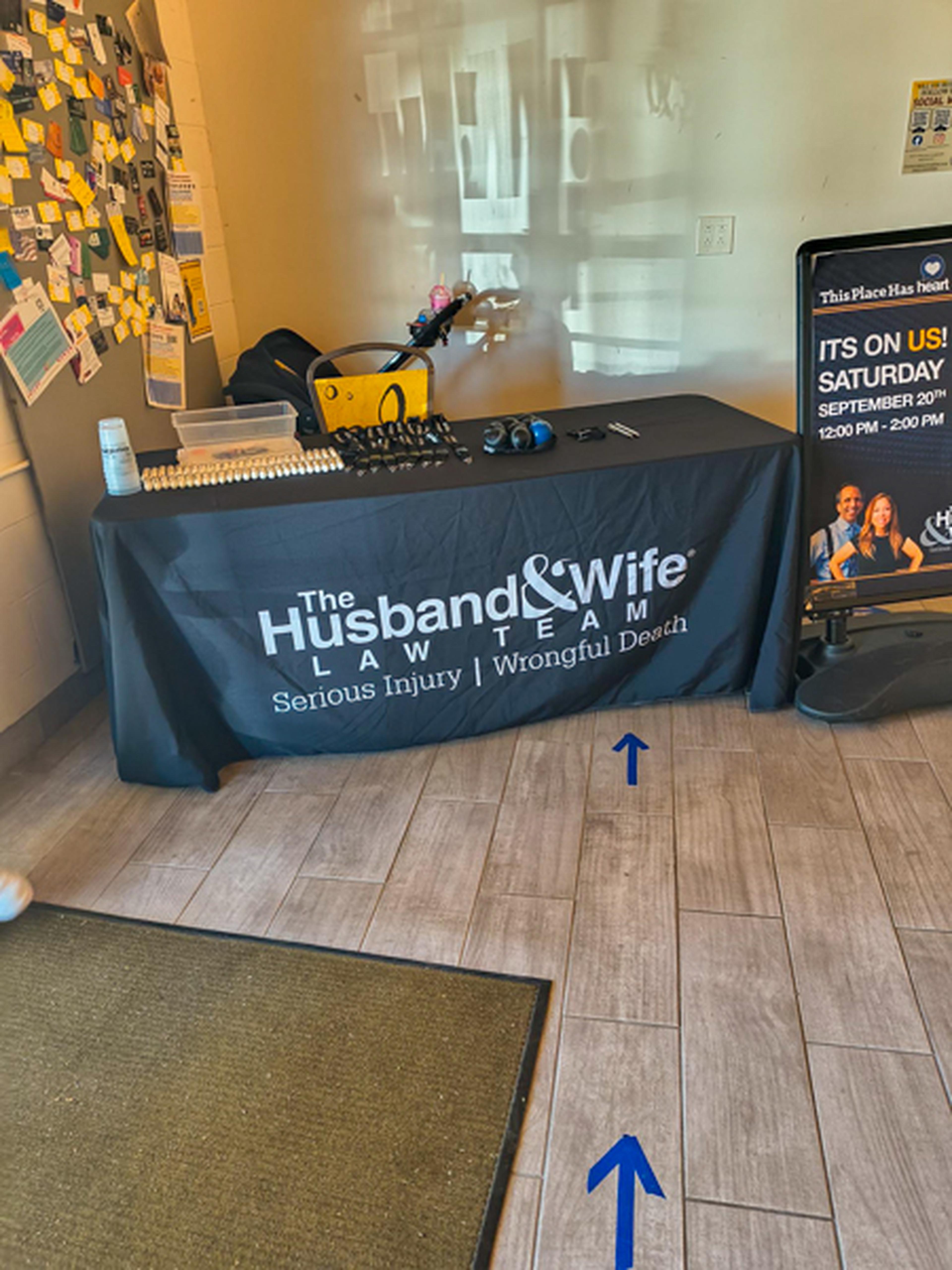 A branded Husband & Wife Law Team table with branded giveaways on it and a sign besides it for the event