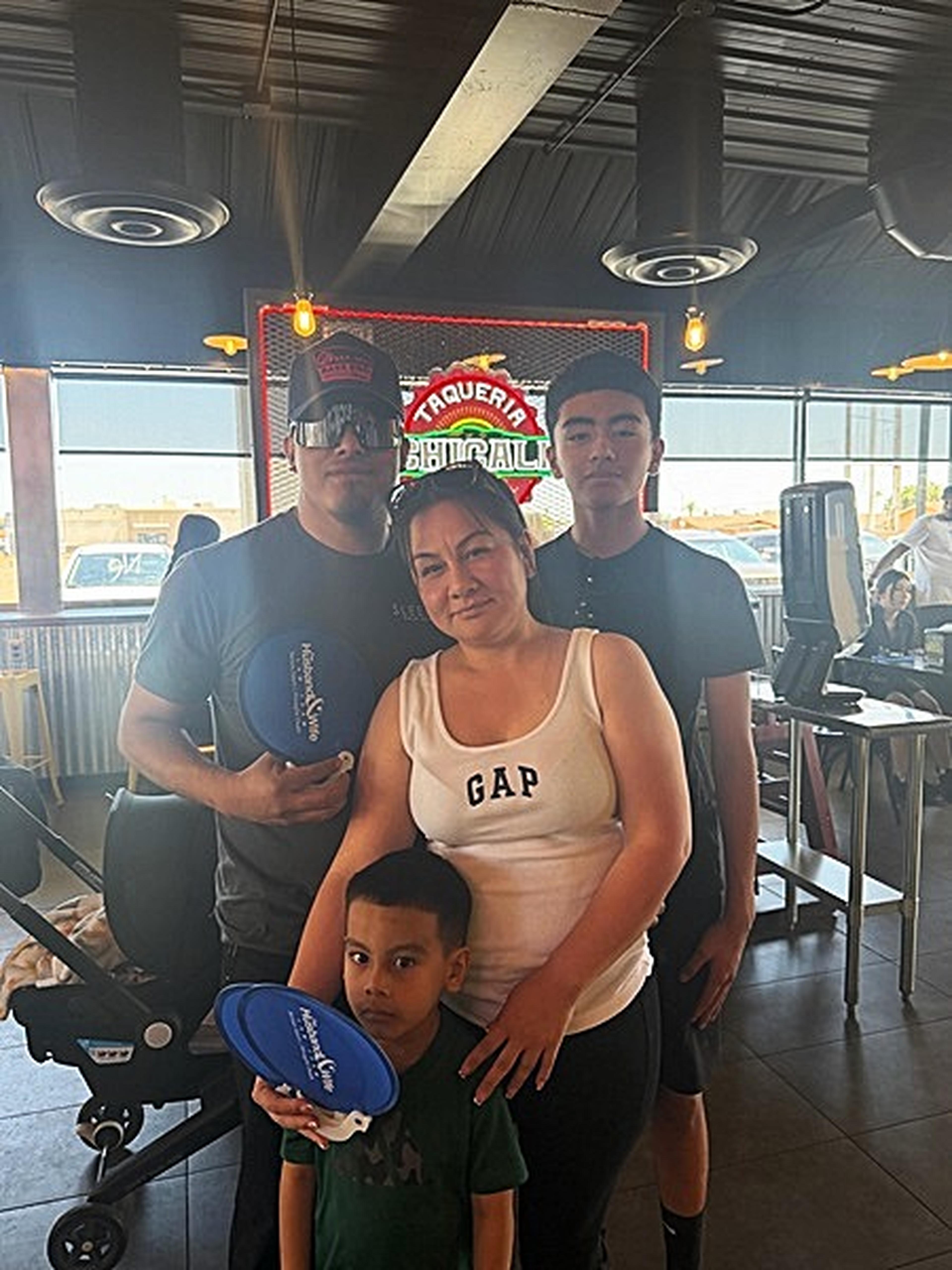 A family of four poses inside Taqueria Chicali, with neon signs and dining tables glowing in the background.