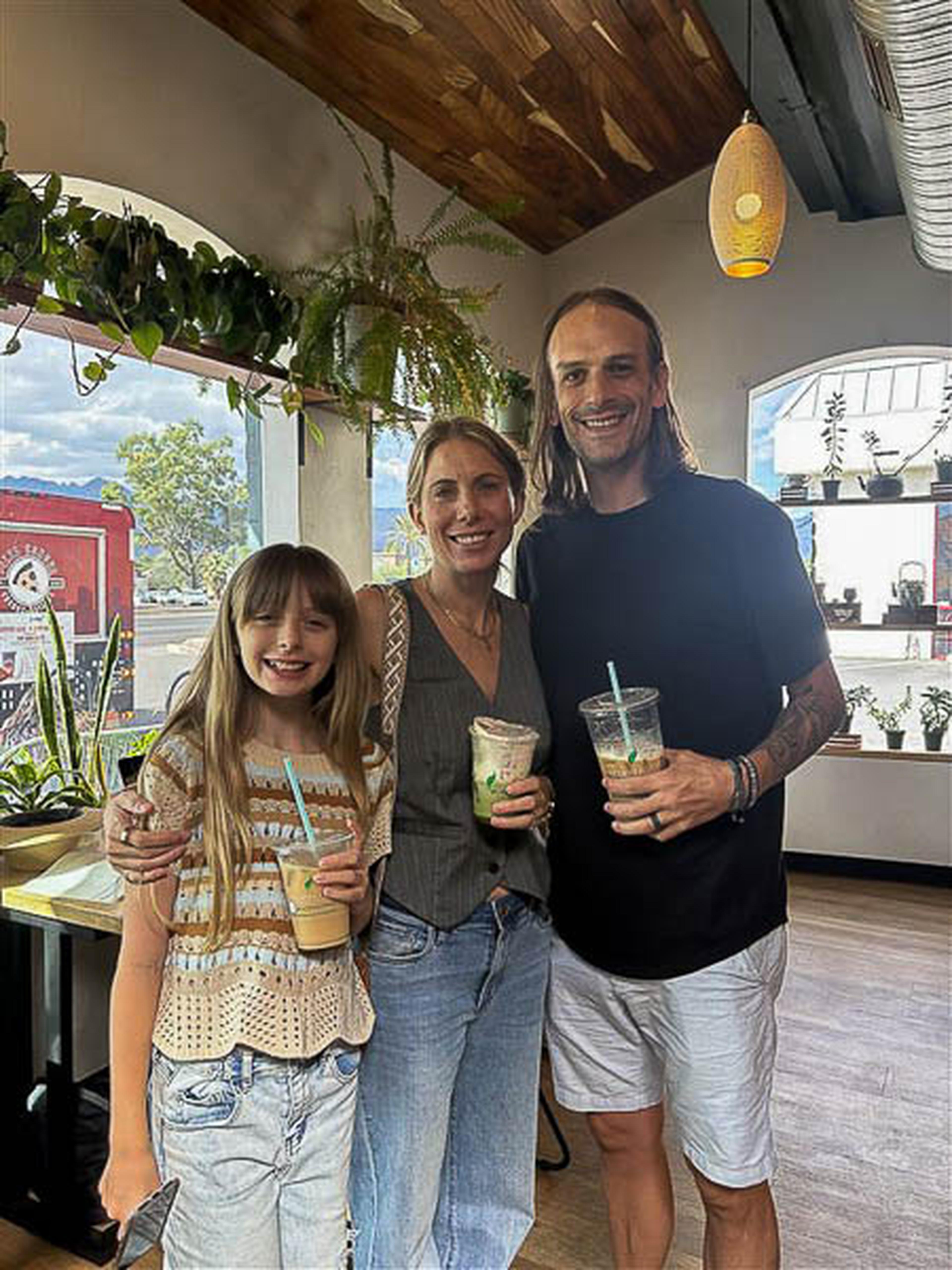 A cheerful trio shows off their drinks at Scented Leaf, surrounded by overhead greenery and a bright window backdrop.