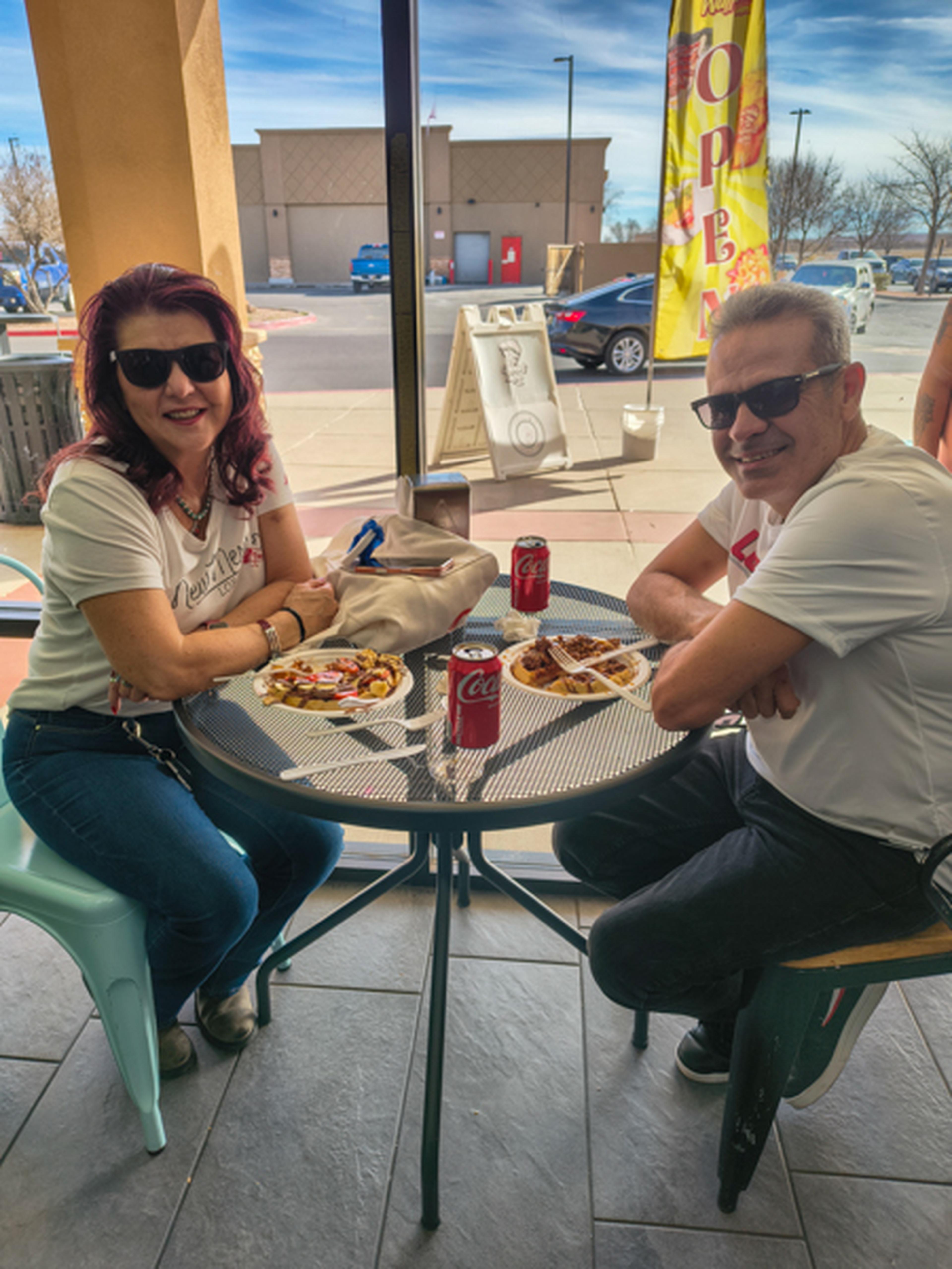 At Crepes and Waffles, a cheerful pair wearing sunglasses relaxes over a table filled with drinks and freshly served dishes.ood on plates in front of them.