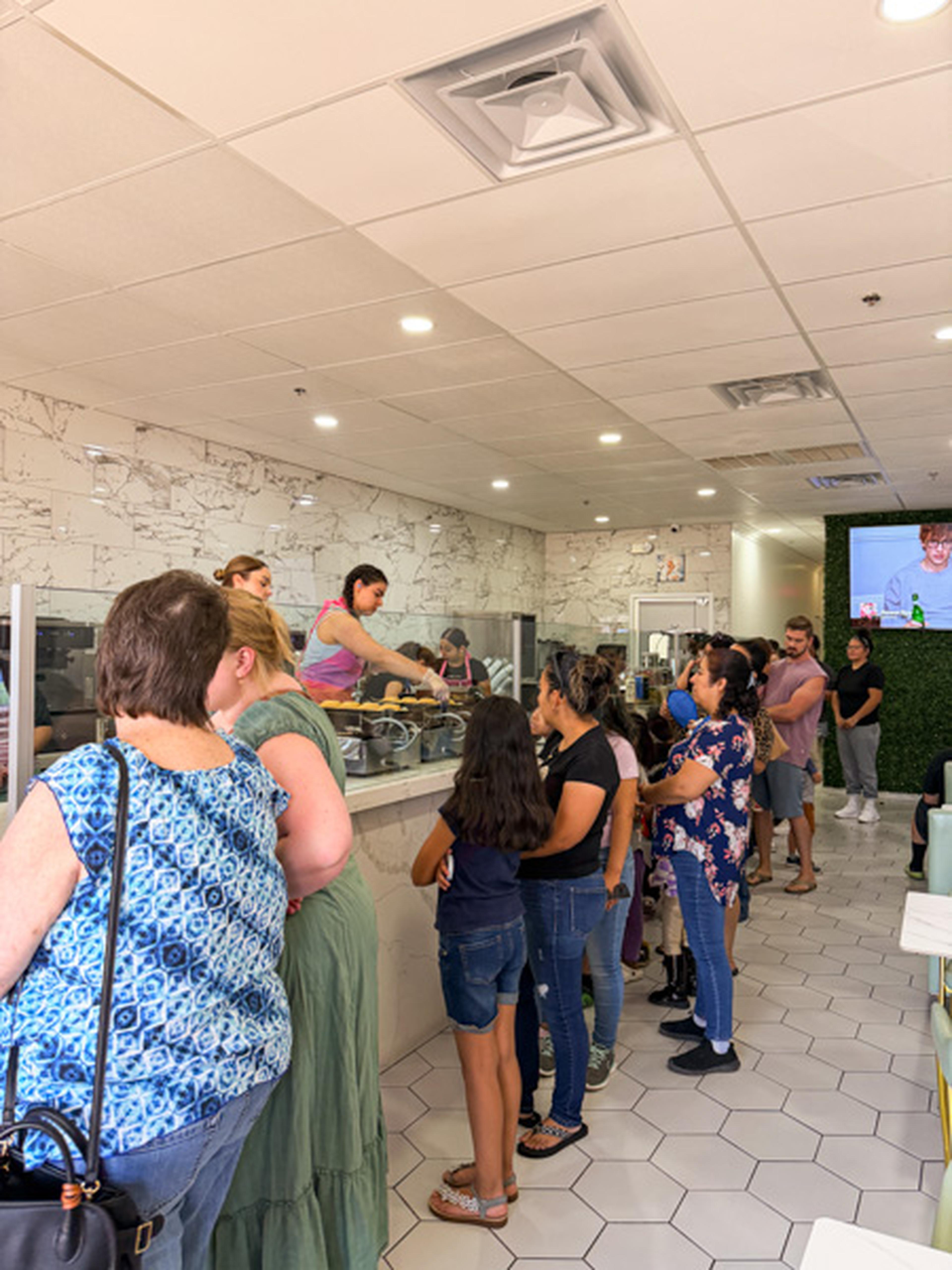 Guests wait in line at Iced Out Ice Cream, surrounded by light wood and marble décor.