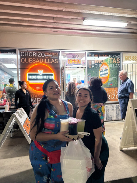 So happy to enjoy a free taco dinner with us! Two women smiling and holding drinks outside a taco shop at night.