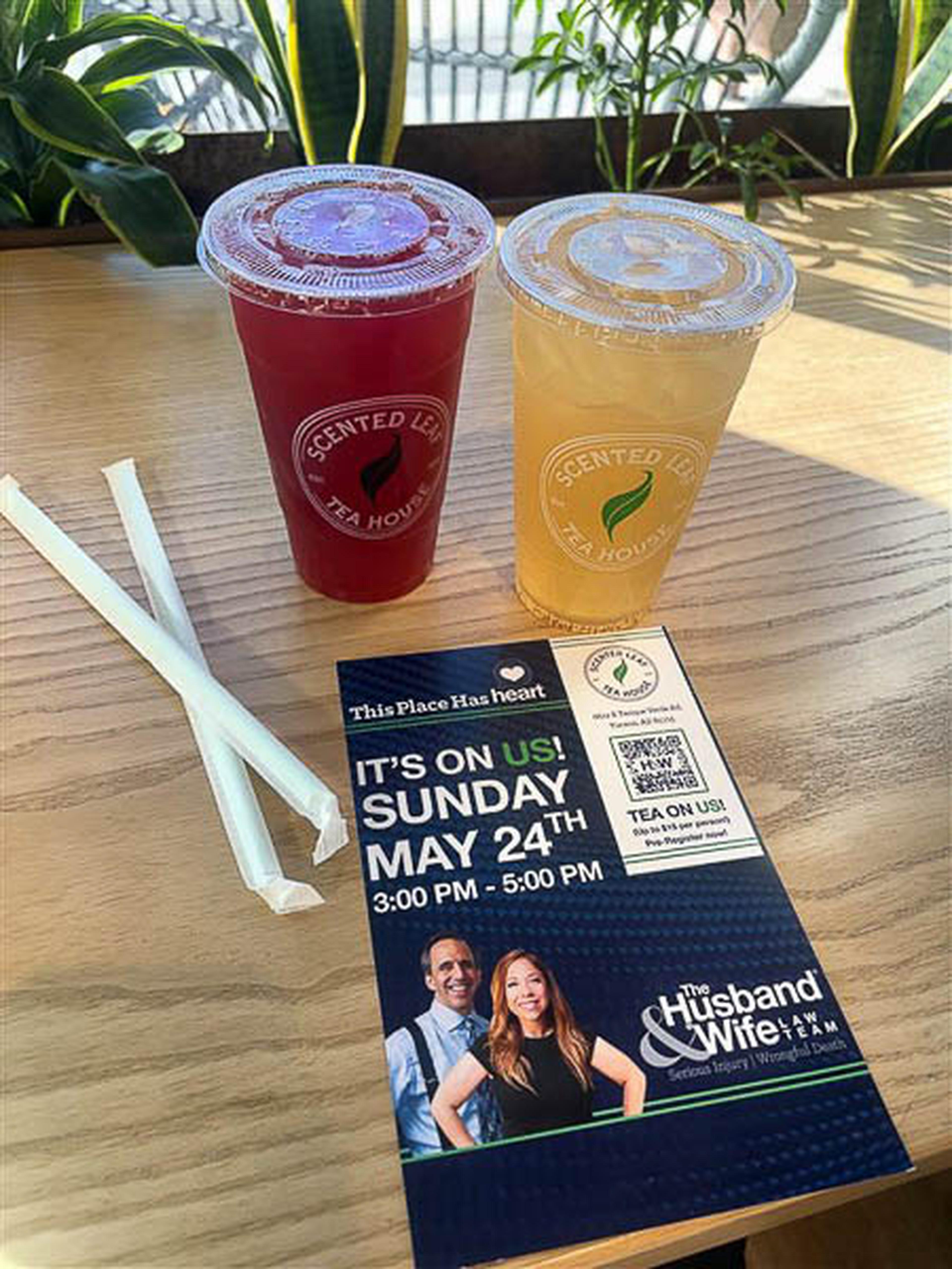 Two cups of iced tea sit on a wooden table beside a flyer advertising a free event and discounted drinks from the Husband & Wife Law Team.