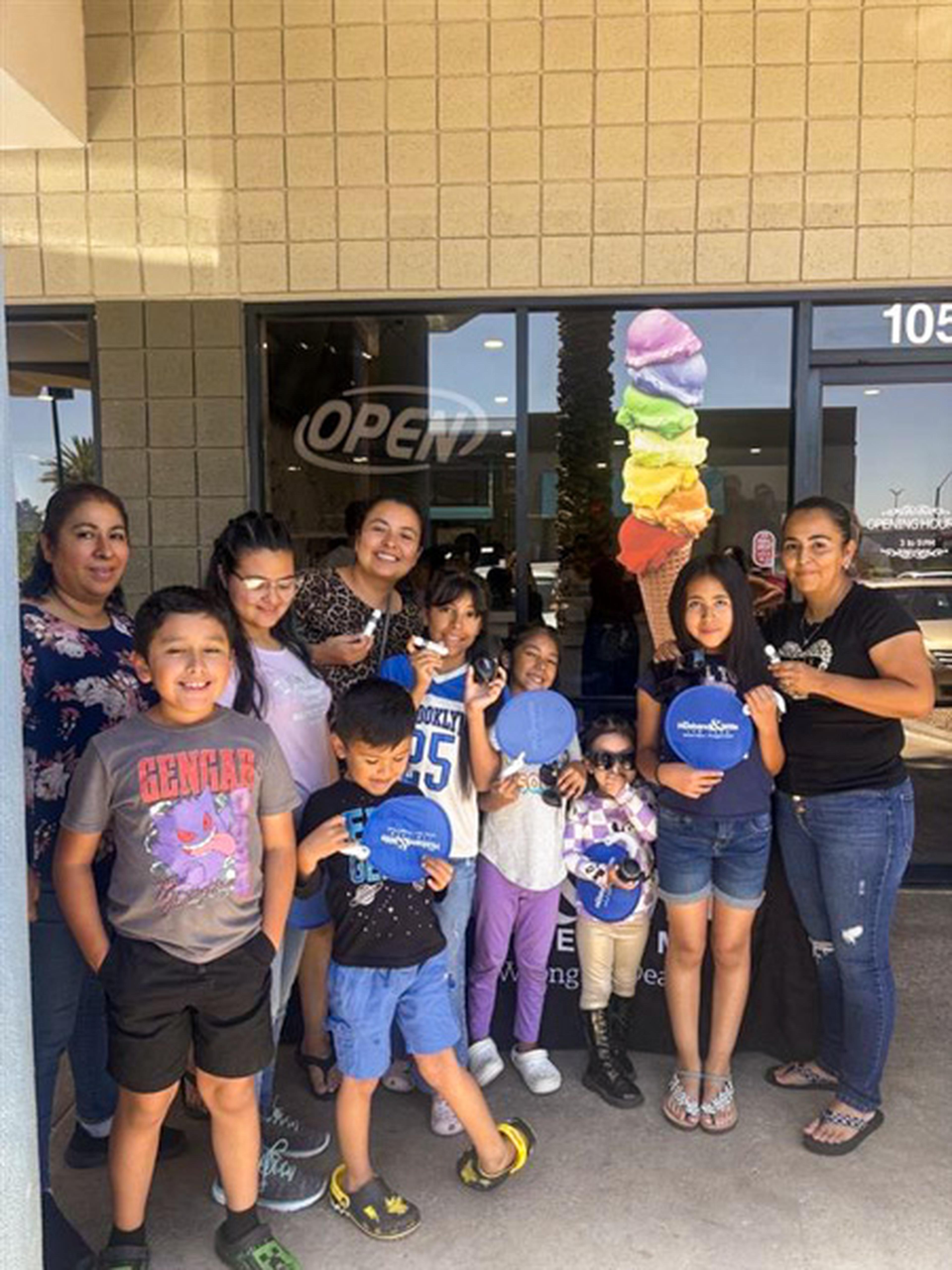 Smiling families and community members pose outside the HEART event in Peoria, holding up bright Husband & Wife Law Team promotional fans.