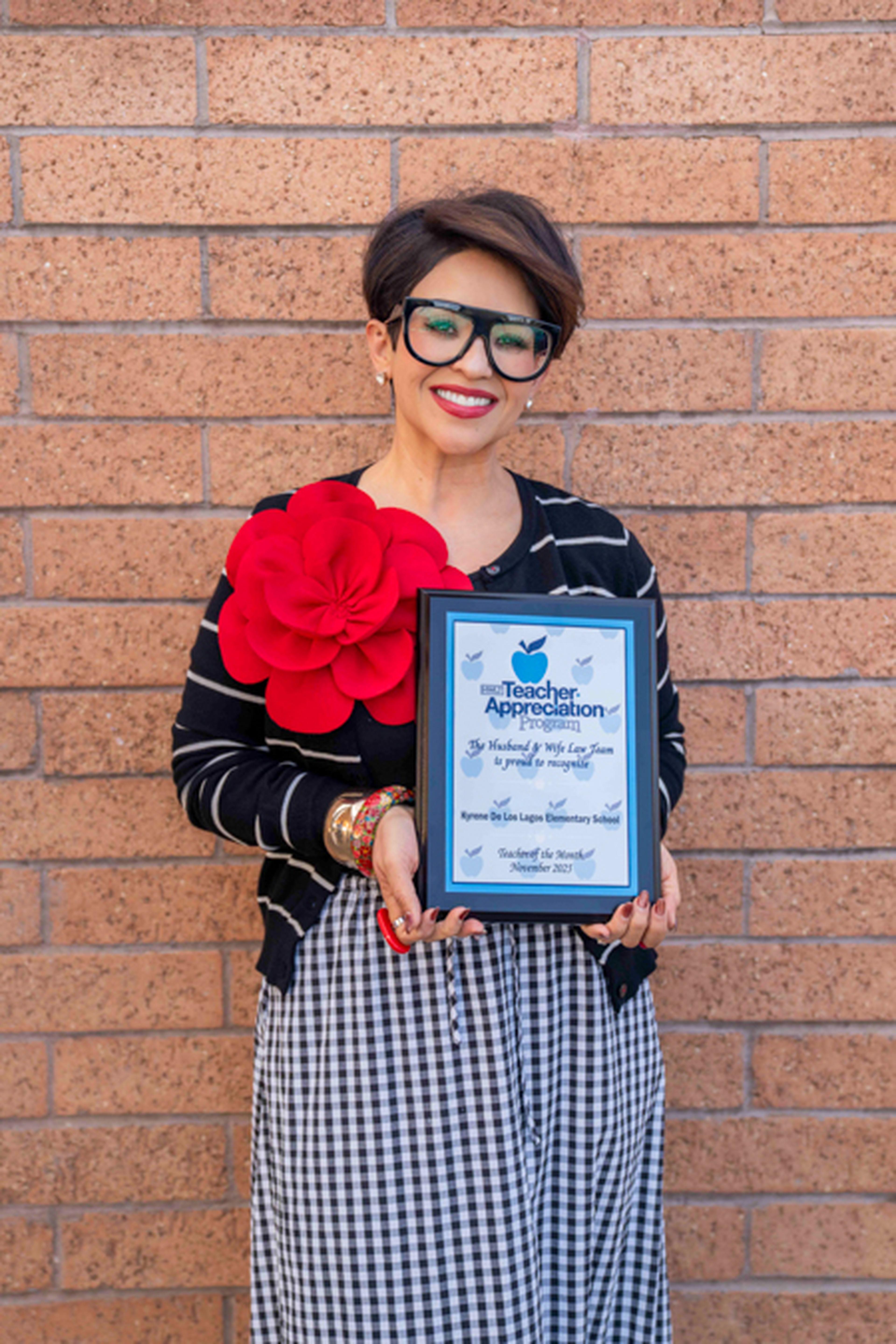 Teacher stands in front of school's wall holding her Teacher Appreciation plaque
