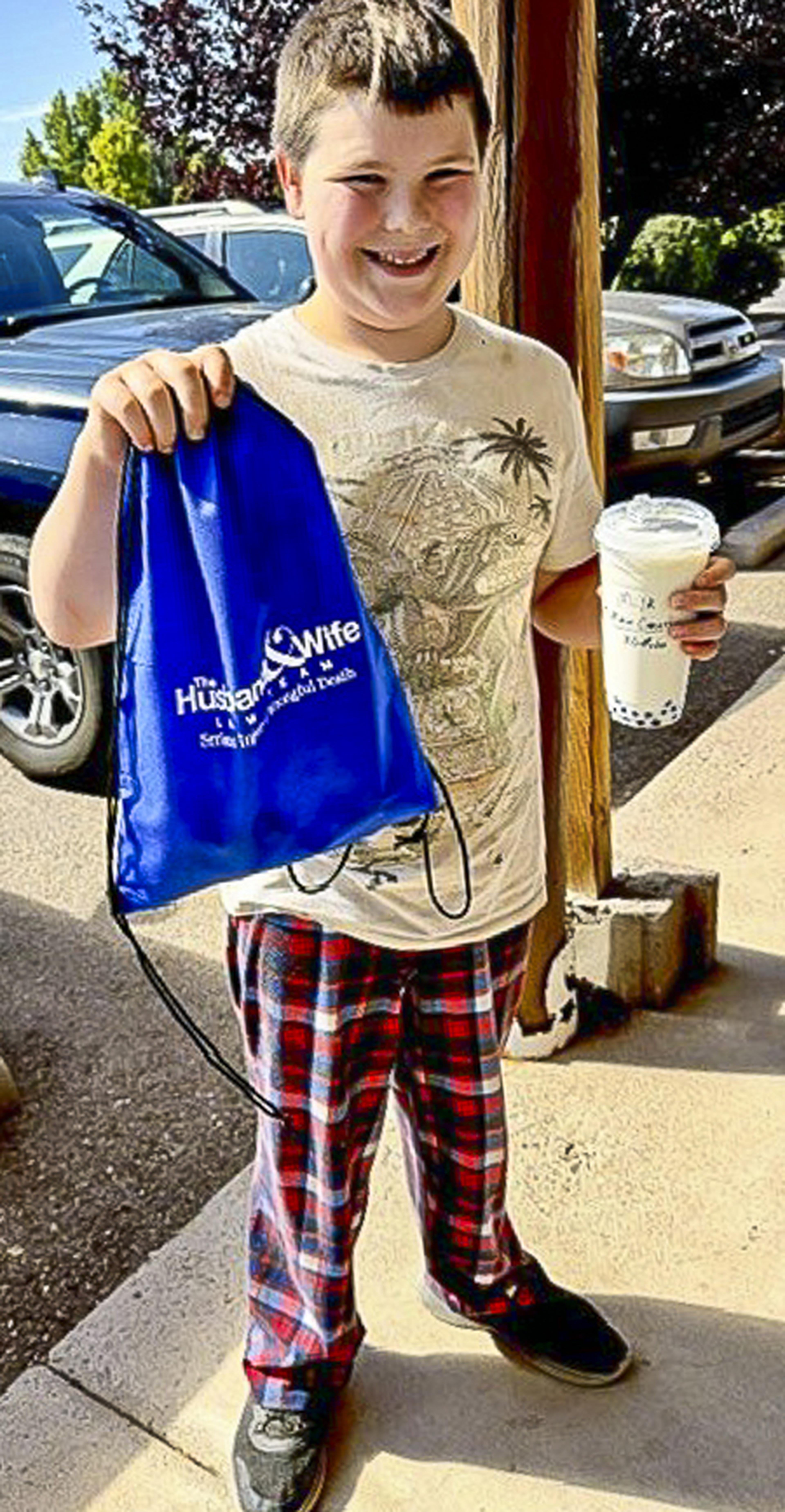 A smiling young boy enjoys a refreshing Route 66 drink while proudly carrying his Husband & Wife Law Team drawstring bag during a fun community event.