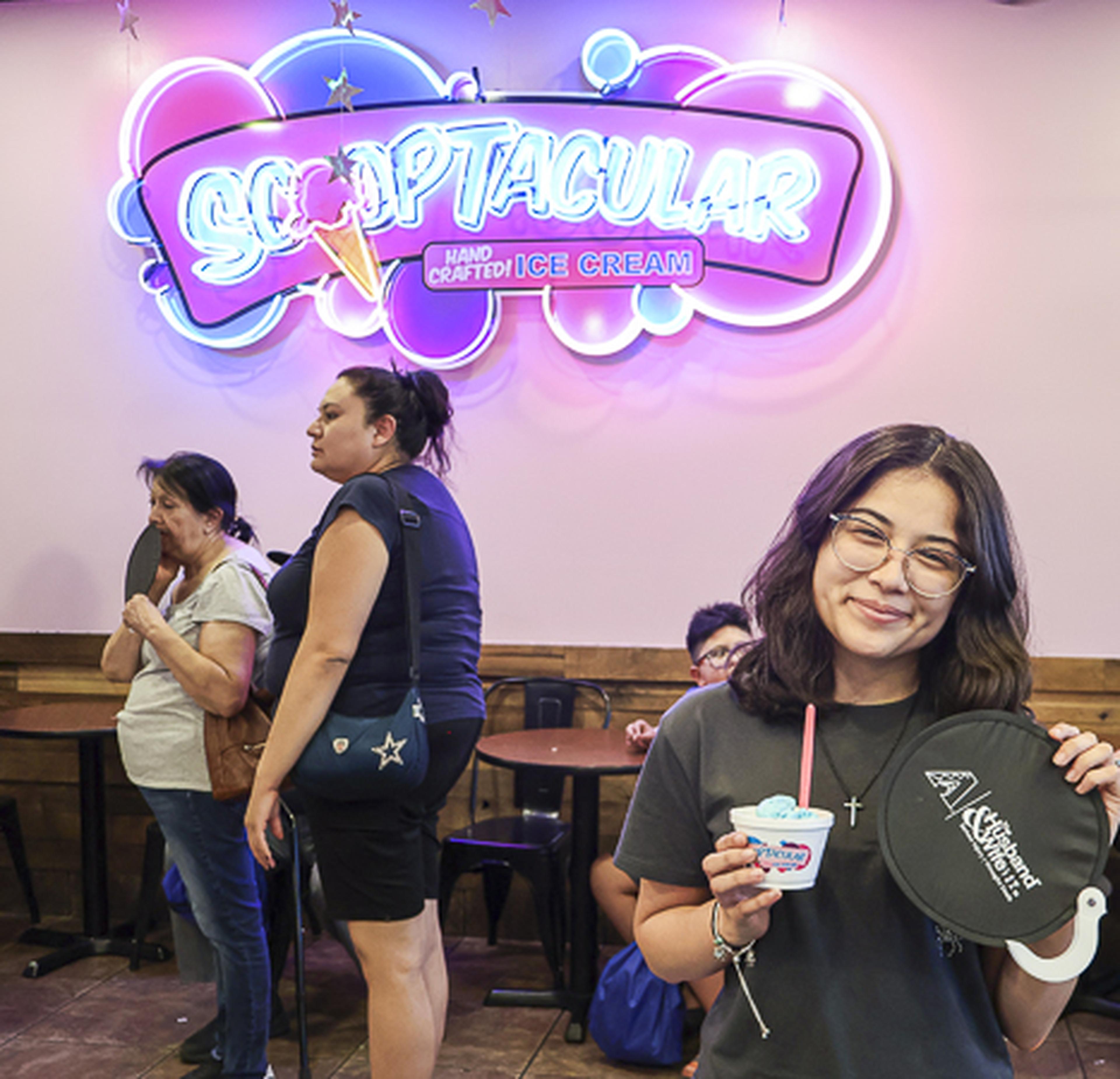 A smiling attendee enjoys a scoop of ice cream while holding a Husband & Wife Law Team fan at the SCOOPTACULAR HEART Event.