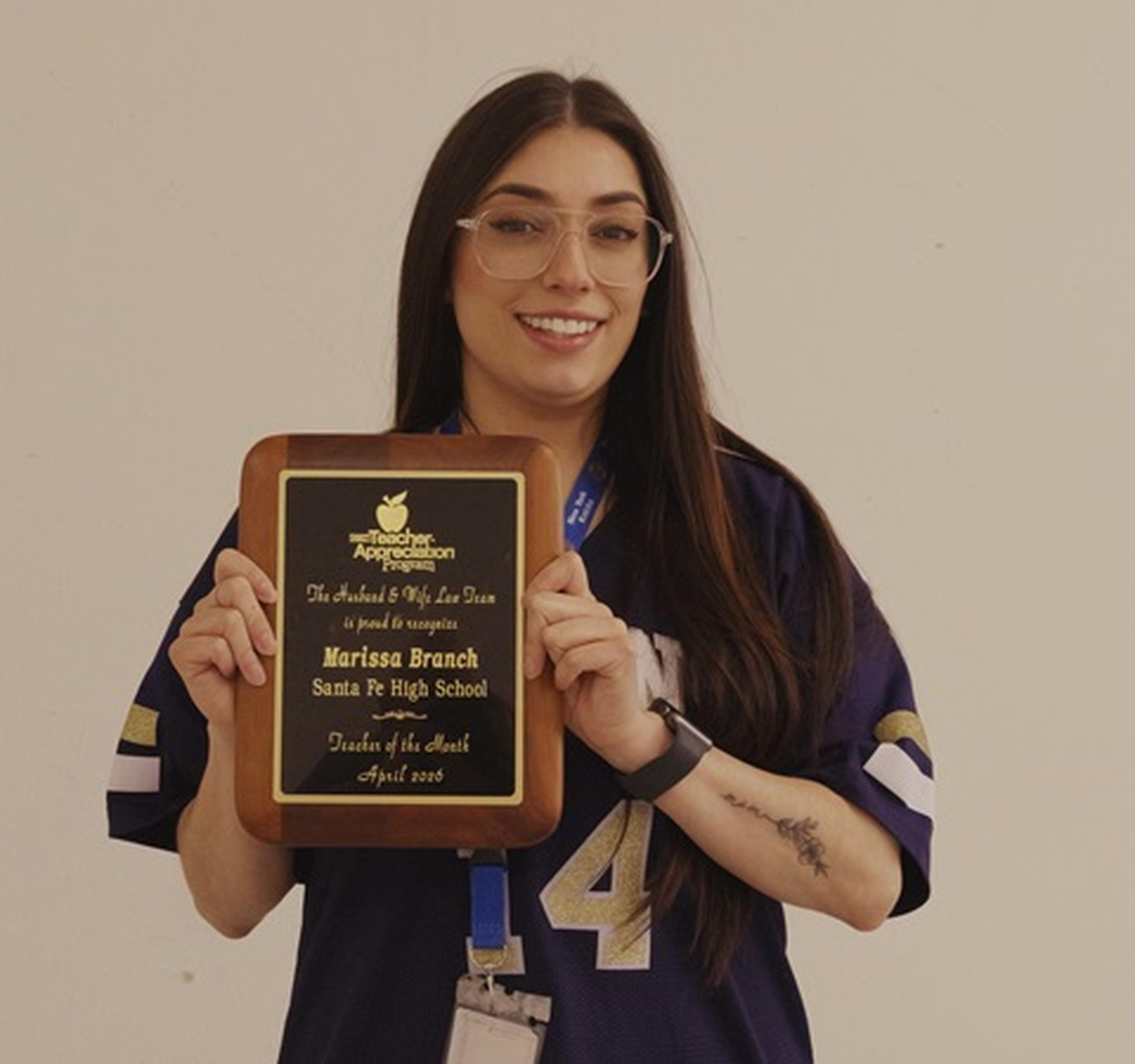 Ms. Branch smiles as she holds her “Teacher of the Month” plaque from the Husband & Wife Law Team.