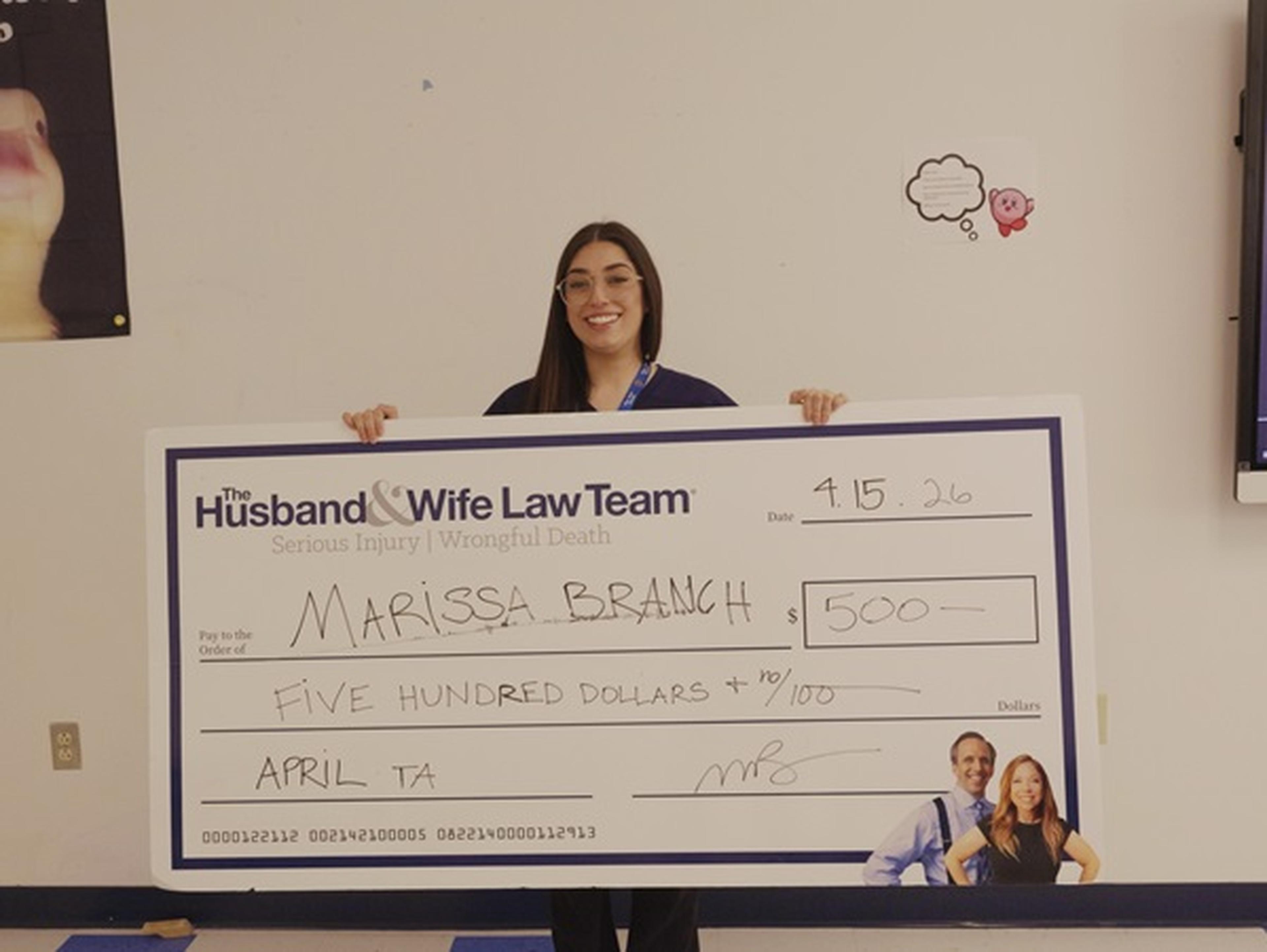 Ms. Branch holding a large novelty check for $500, issued by "Husband & Wife Law Team"