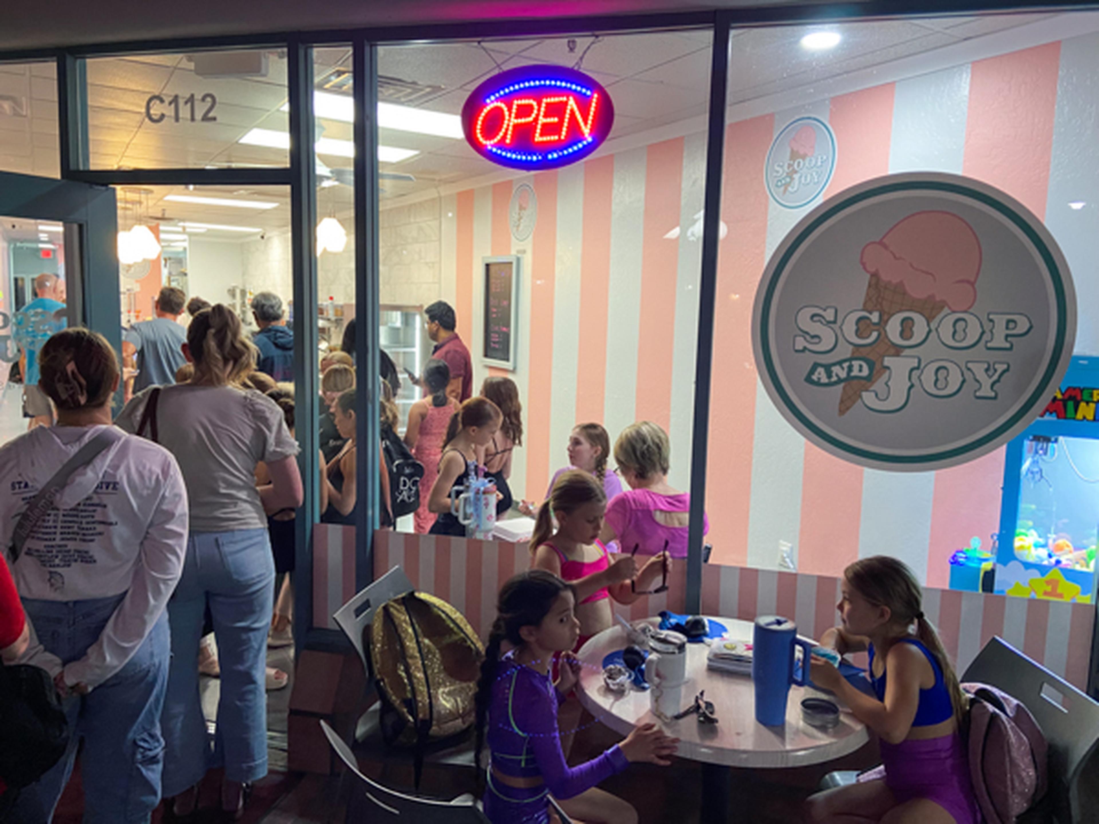 People inside Scoop and Joy ice cream shop. Children sit at a table eating.