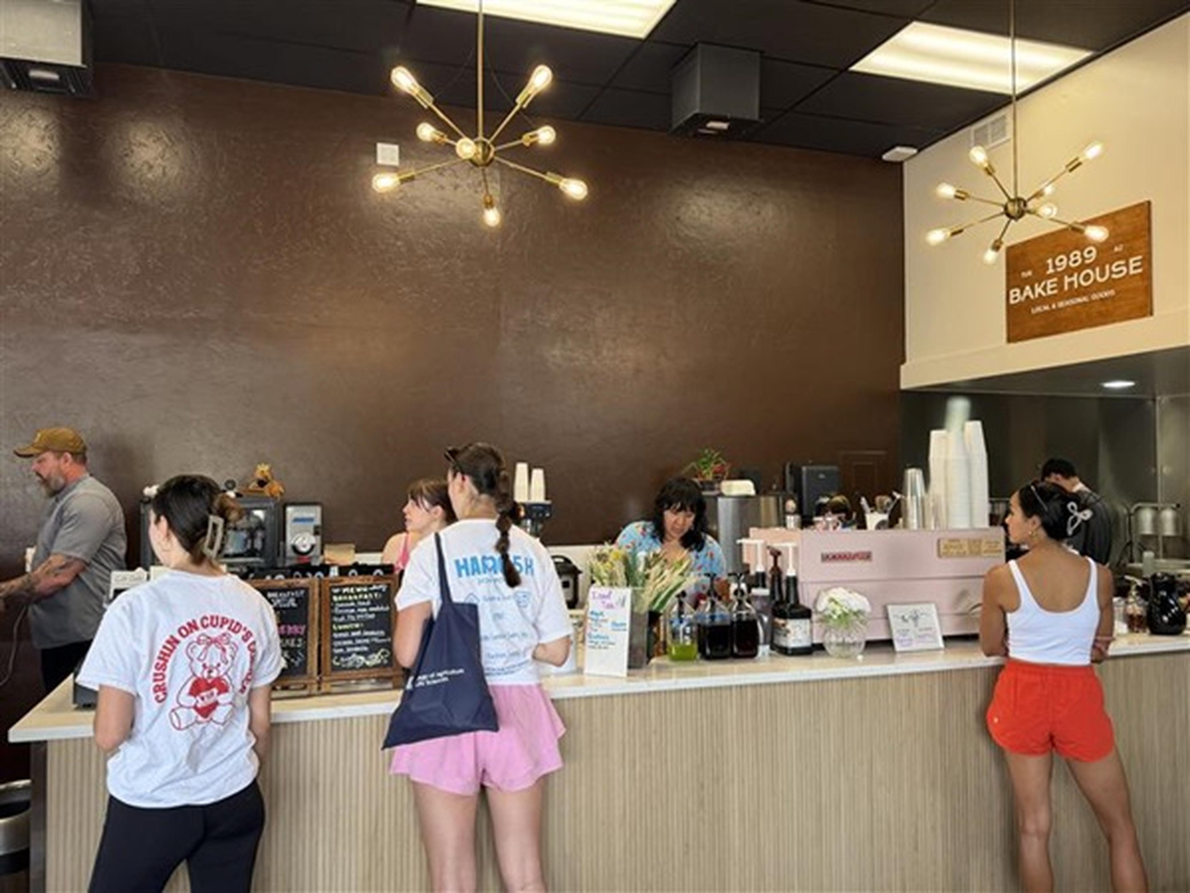 Customers line up at the 1989 Bake House counter beneath modern pendant lights, with the “1989 Bake House” sign displayed on the wall.