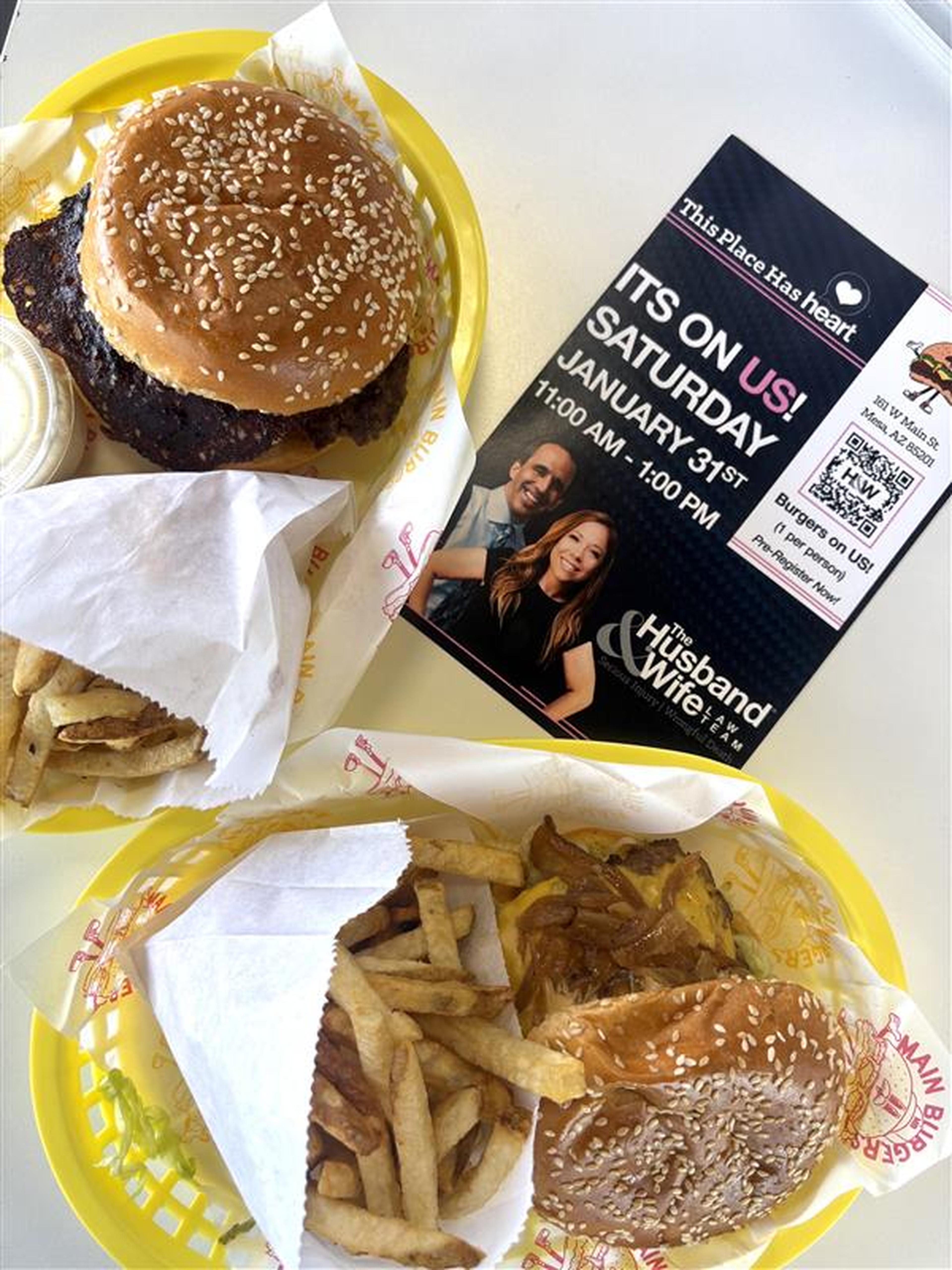 Two baskets with burgers and fries alongside a flyer for a charity event on January 31st featuring the Husband & Wife Law Team