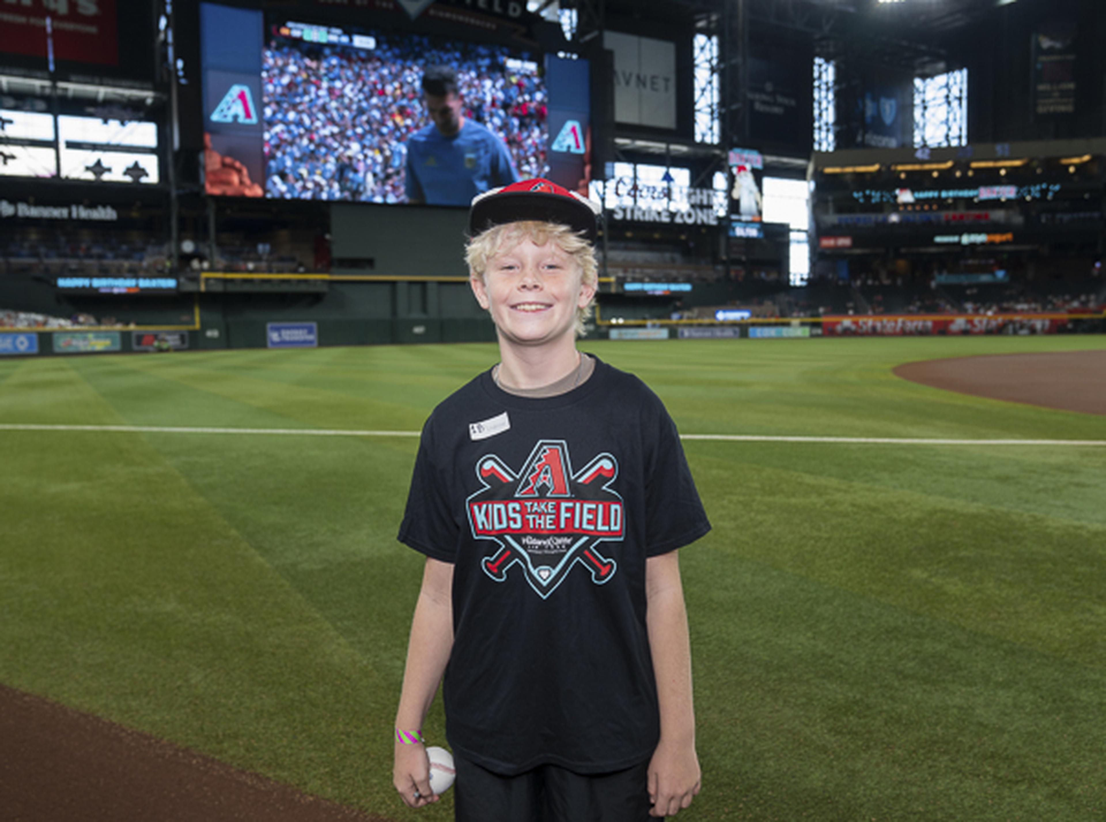 Big-league dreams start here. A smiling Kids Take the Field participant poses on Chase Field with baseball in hand and aspirations of playing under the bright lights one day.