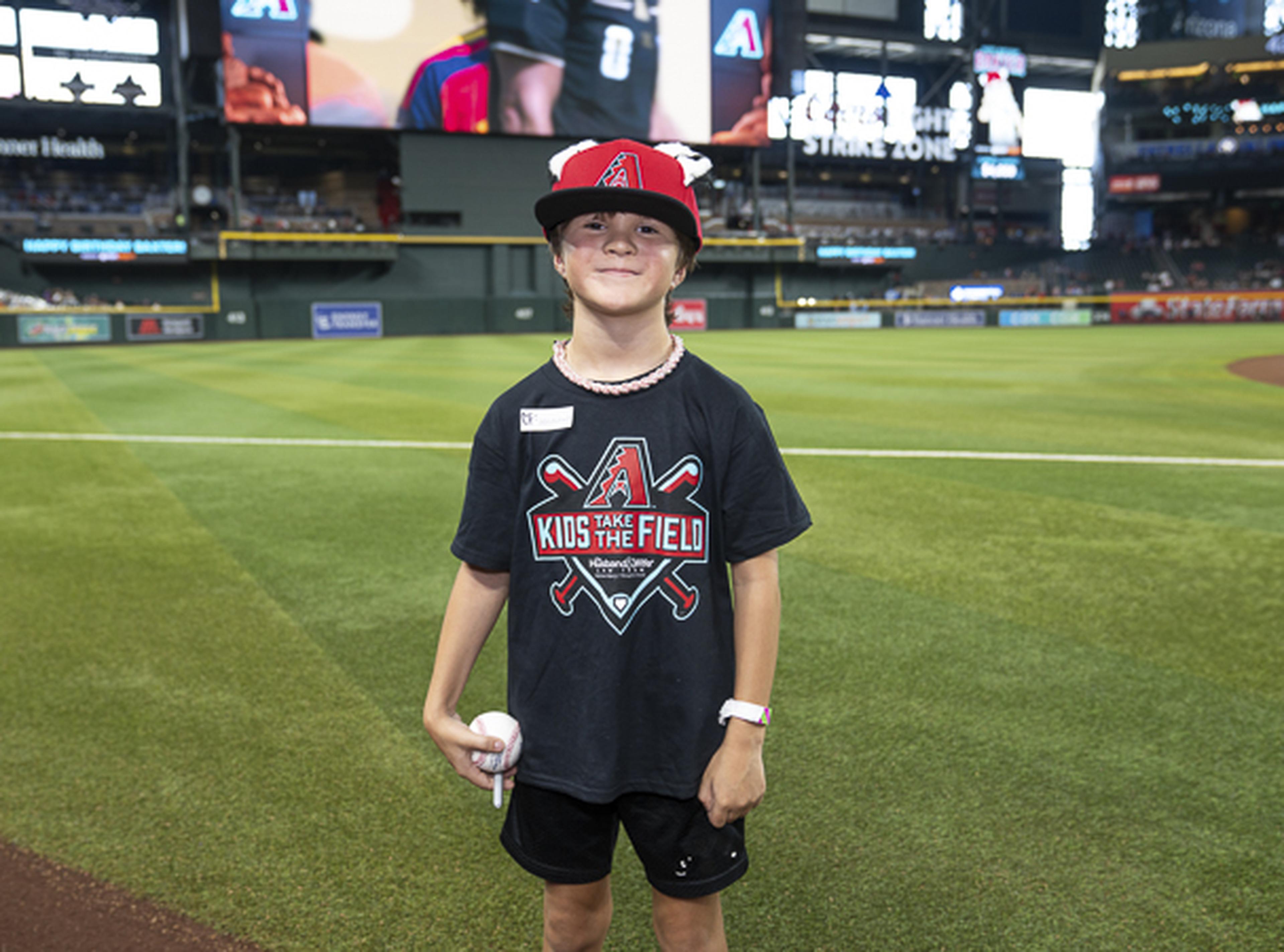 Eyes set on the big leagues, this young baseball fan stands proudly on the field with a baseball in hand, soaking in a once-in-a-lifetime Kids Take the Field experience.