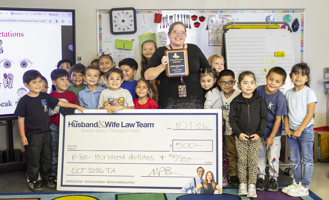 The Husband & Wife Law Team honors Mrs. Warren with a $500 Teacher of the Month award, celebrating her dedication and positive impact on her students. Mrs. Warren celebrates her Teacher of the Month recognition alongside her students, proudly displaying a $500 award and plaque from the Husband & Wife Law Team.