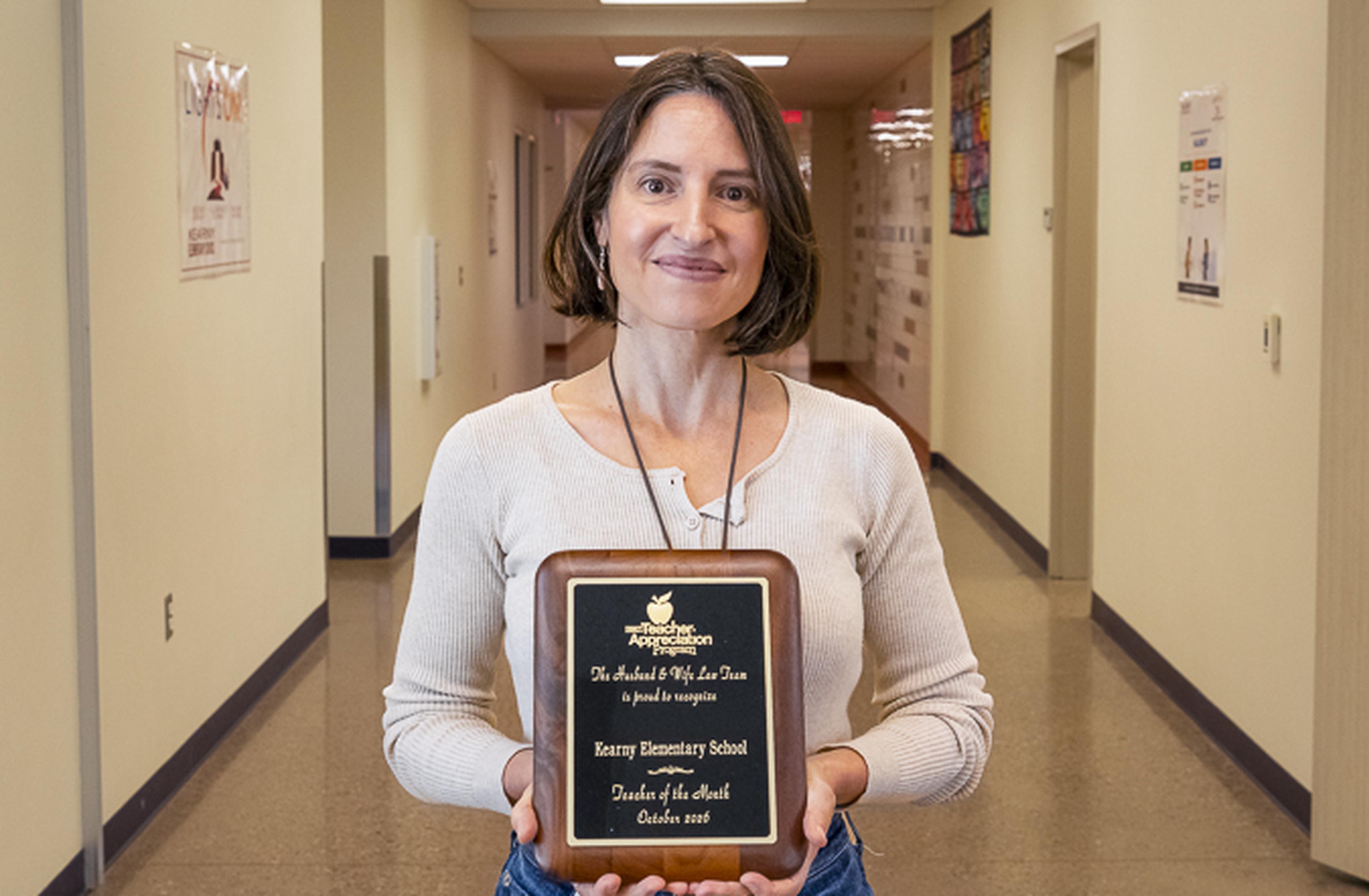 Mrs. Vargas-Portley proudly displays her Teacher of the Month award at Kenny Elementary School, celebrating her dedication and positive impact on students.