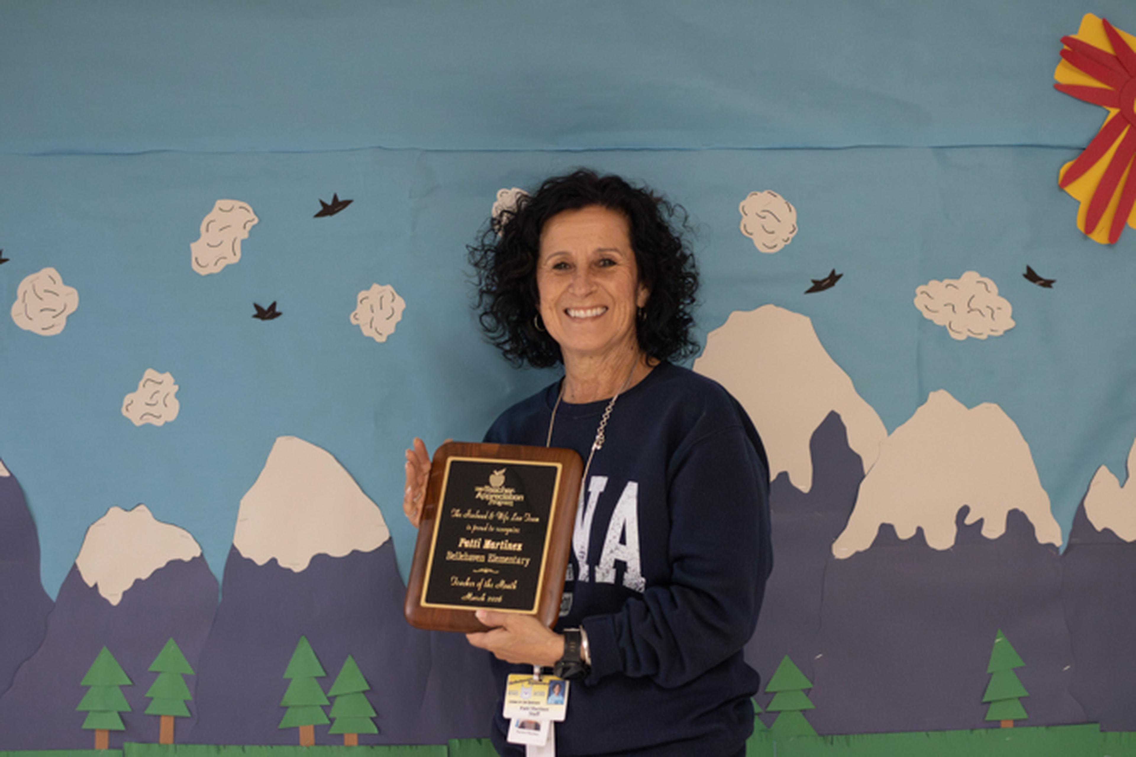 Ms. Martinez smiling and holding a Teacher Appreciation Award from The Husband & Wife Law Team