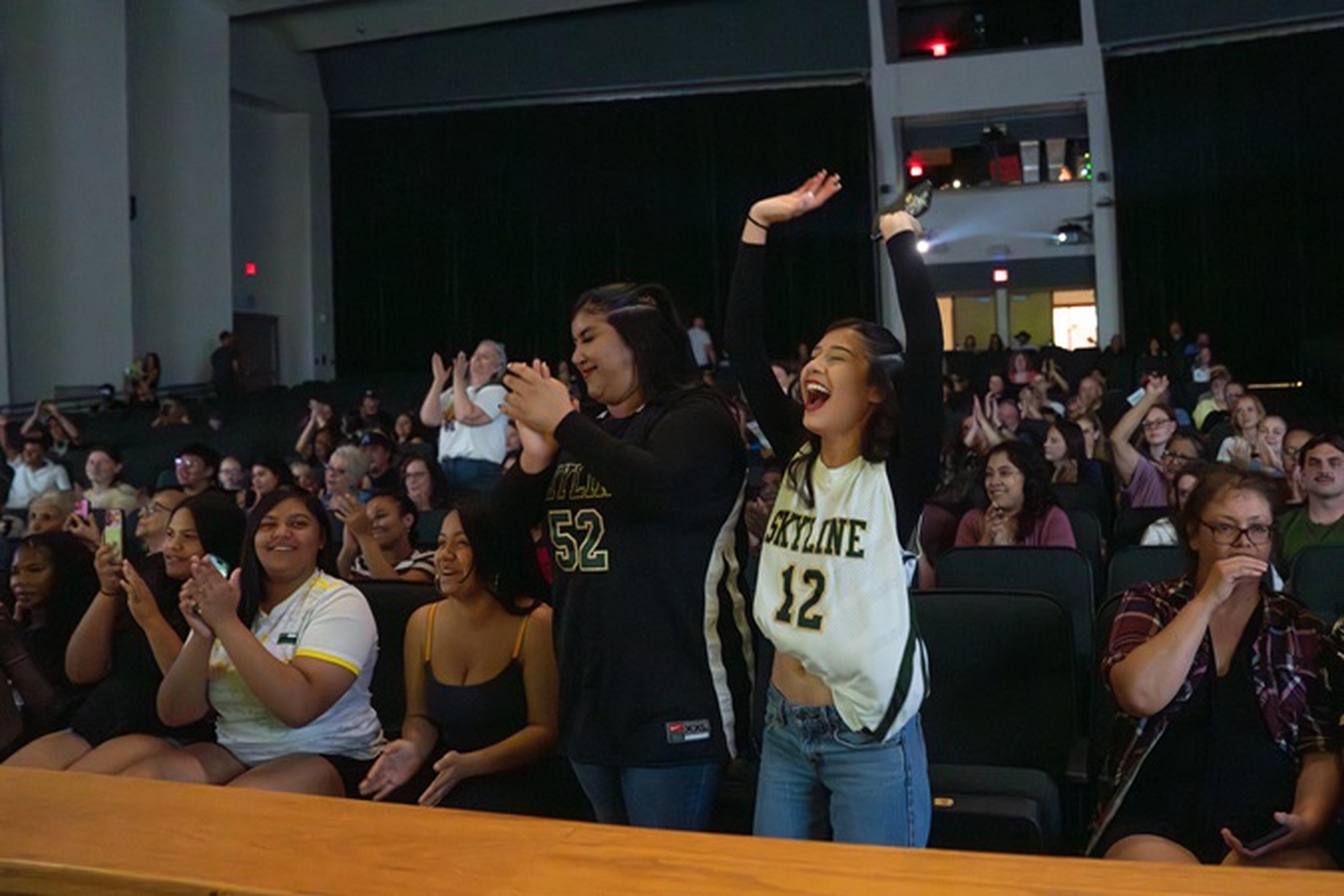 Students cheering and clapping, celebrating enthusiastically. when Ms. Johnson is presented with the Husband and Wife Teacher Appreciation Award