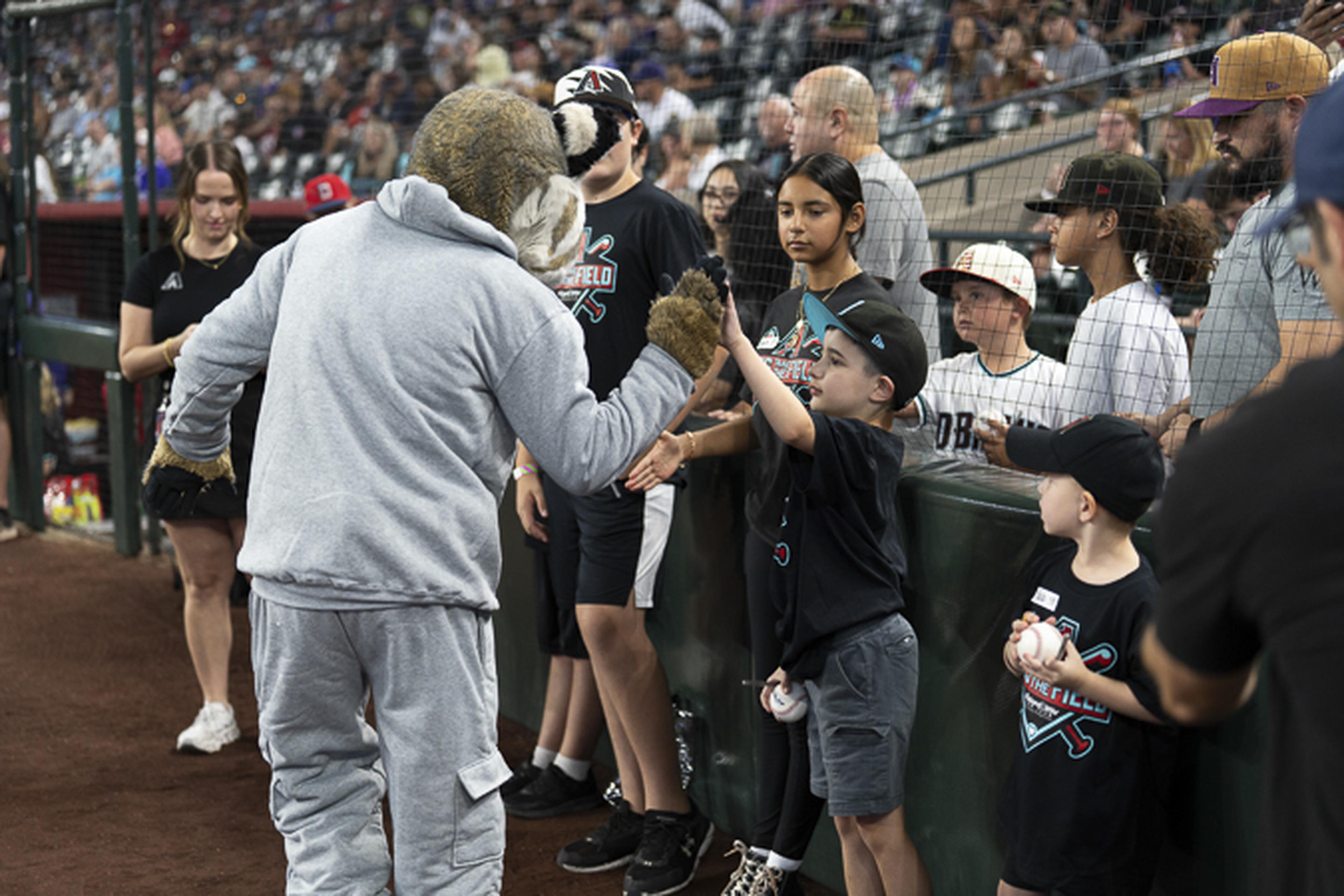 Baxter, the Arizona Diamondbacks mascot, shares a high-five with a young fan near the field, creating a memorable moment at the ballpark.