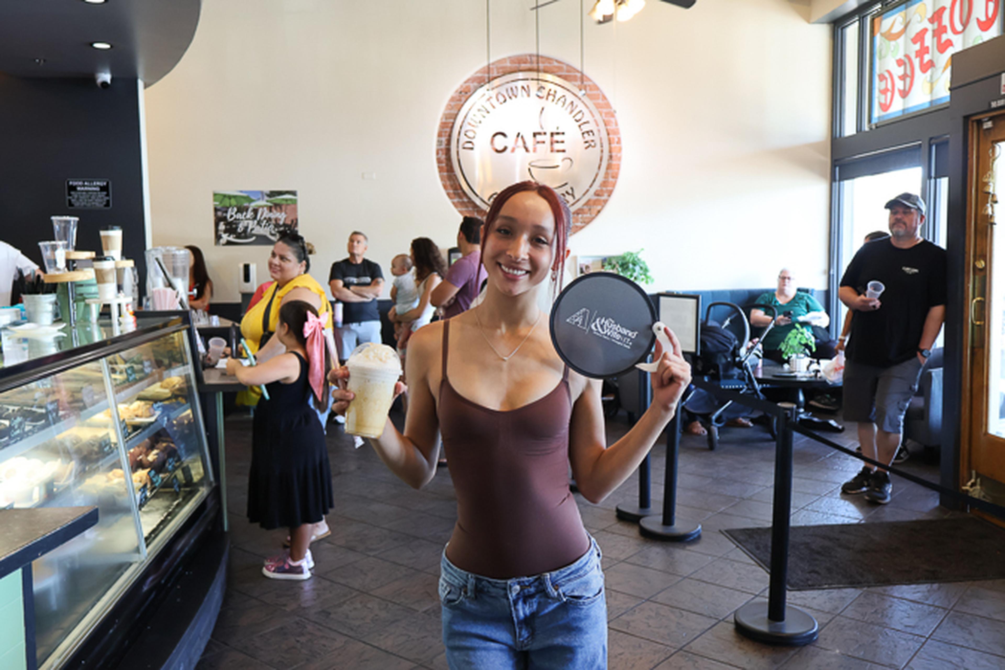 An attendee enjoys a drink at Downtown Chandler Cafe & Bakery while showing off a Husband & Wife Law Team fan during a community-focused HEART event.