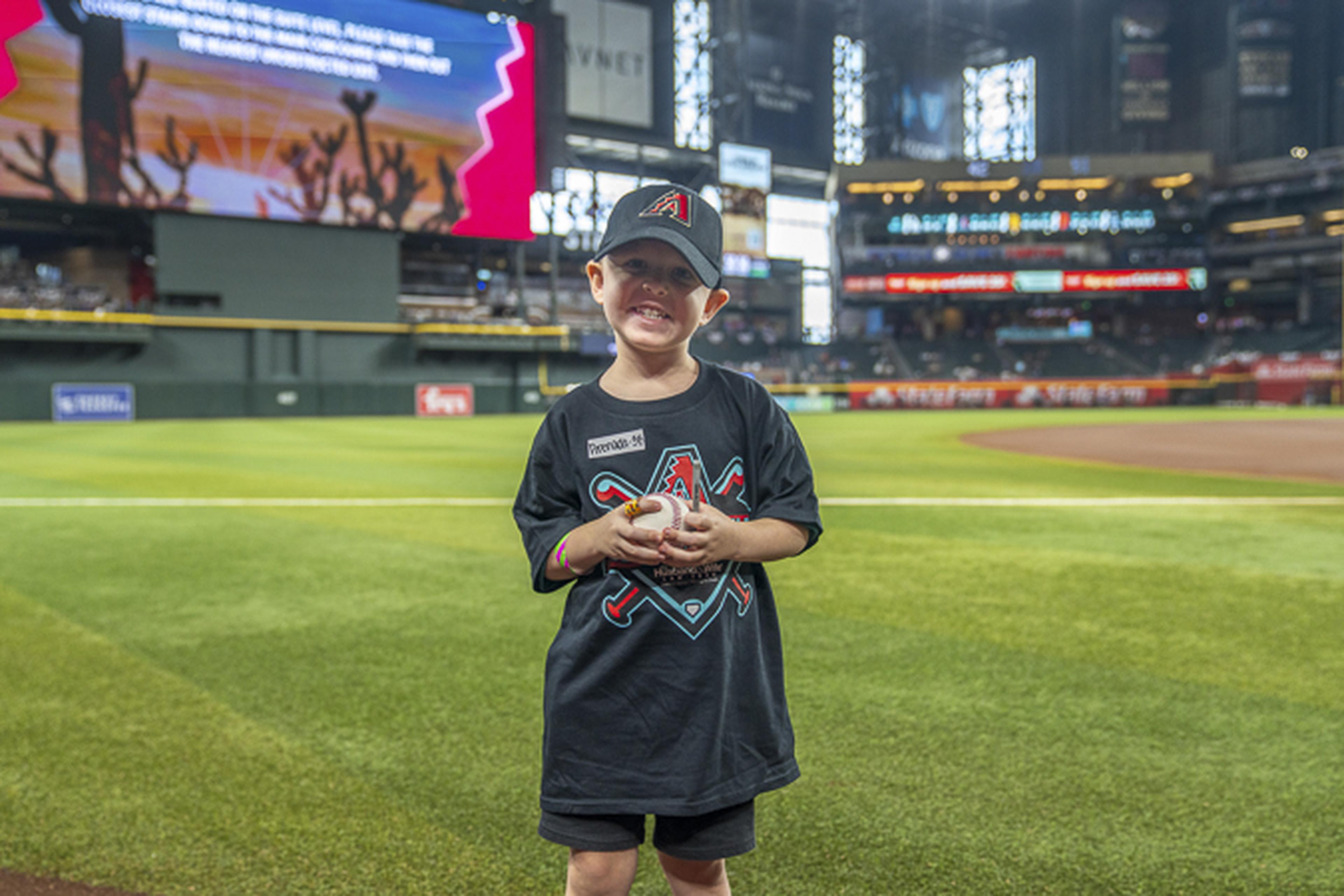 A young Arizona Diamondbacks fan proudly holds a baseball on the field at Chase Field, creating memories during an unforgettable day at the ballpark.