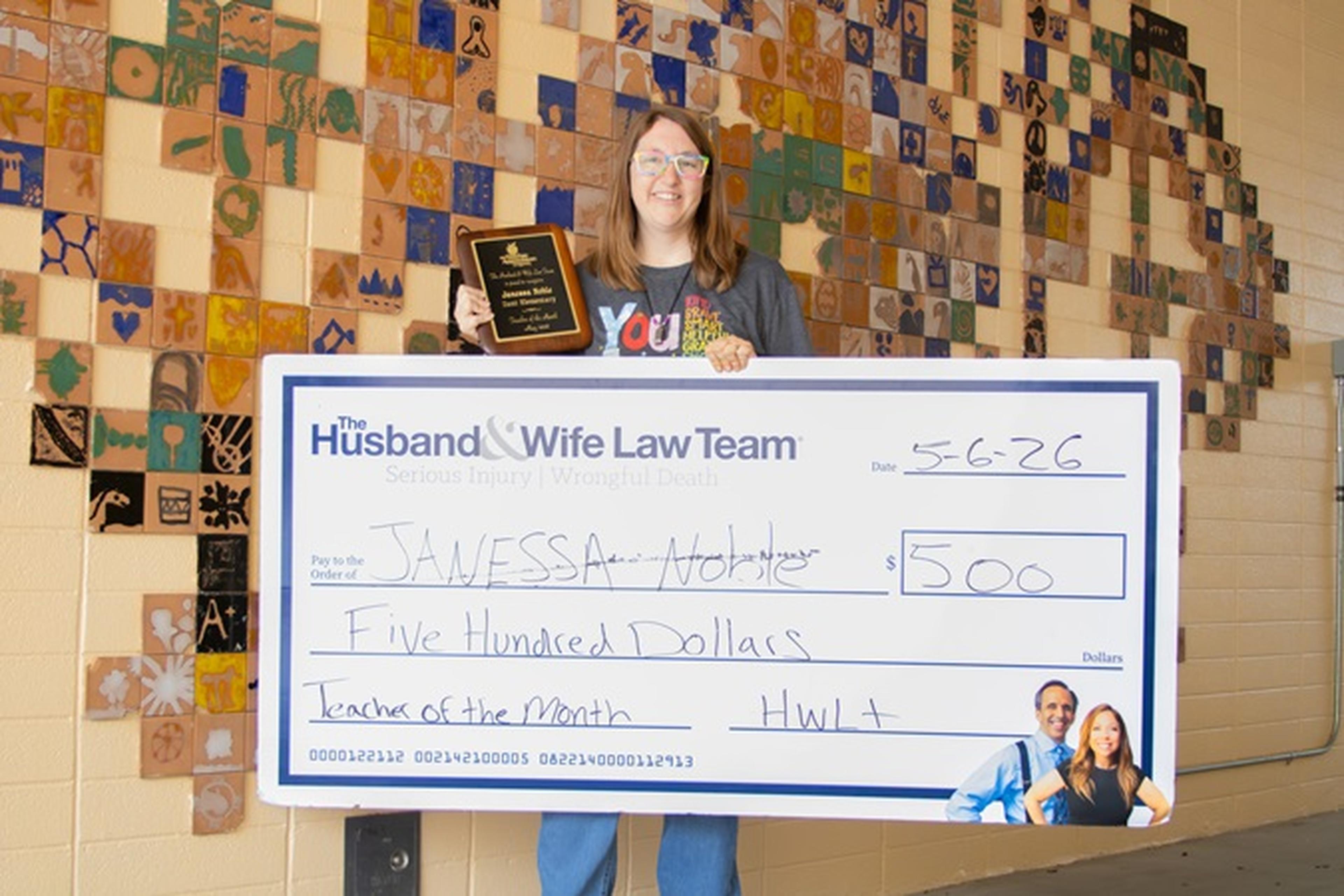 Ms. Noble displays her plaque alongside a large $500 check recognizing her as “Teacher of the Month
