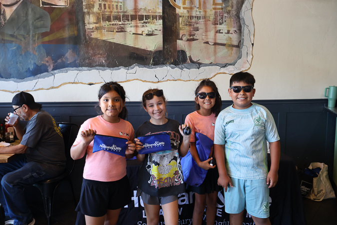 Wearing sunglasses and sharing big smiles, four children pose with Husband & Wife Law Team items at Downtown Chandler Cafe & Bakery, enjoying a day of family-friendly fun. Four young attendees smile while showing off their Husband & Wife Law Team giveaways at Downtown Chandler Cafe & Bakery during a fun community gathering.
