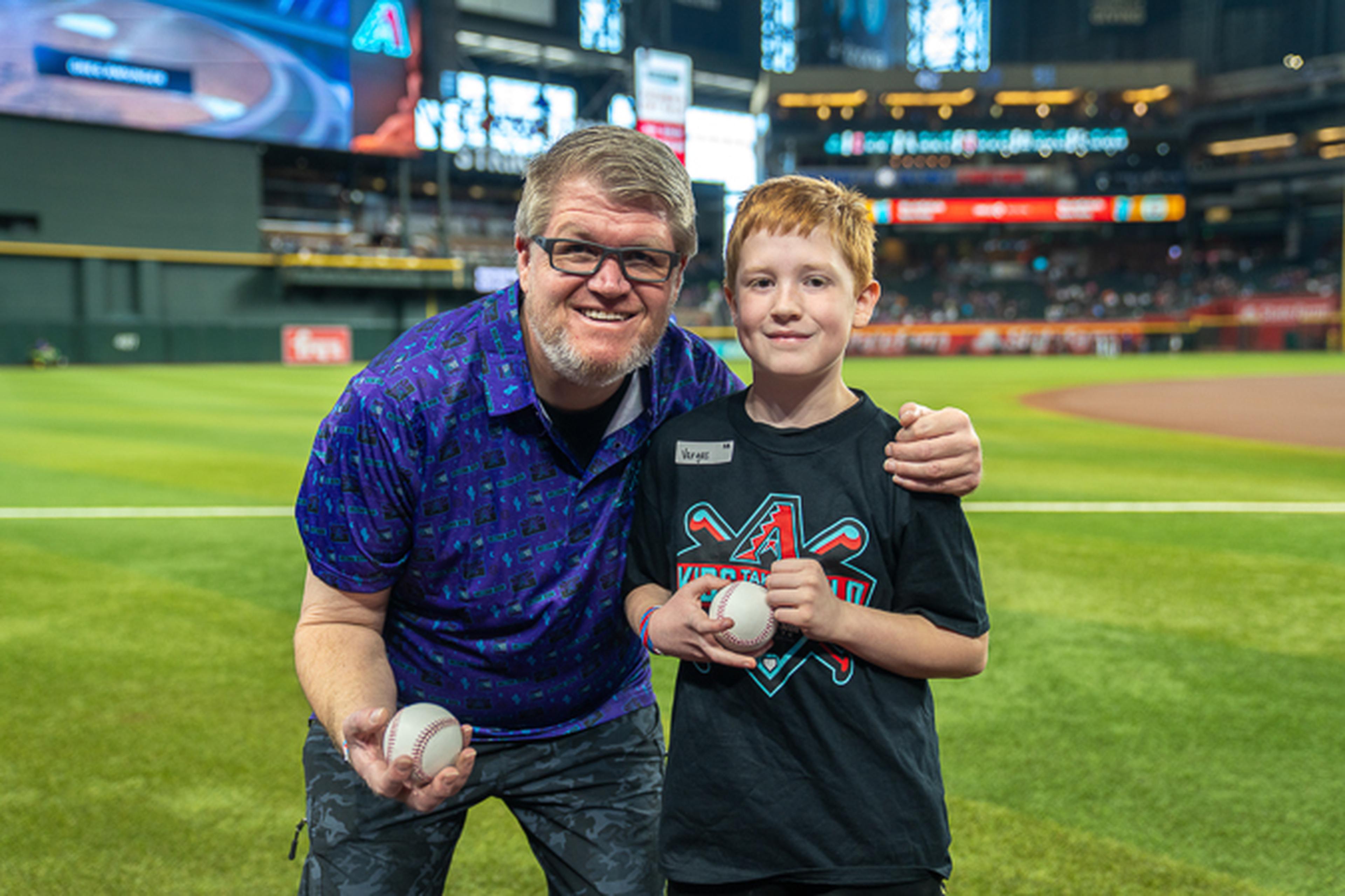 Father and son all smiles at Chase Field before the Sunday ball game, with stadium lights and the scoreboard glowing behind them.
