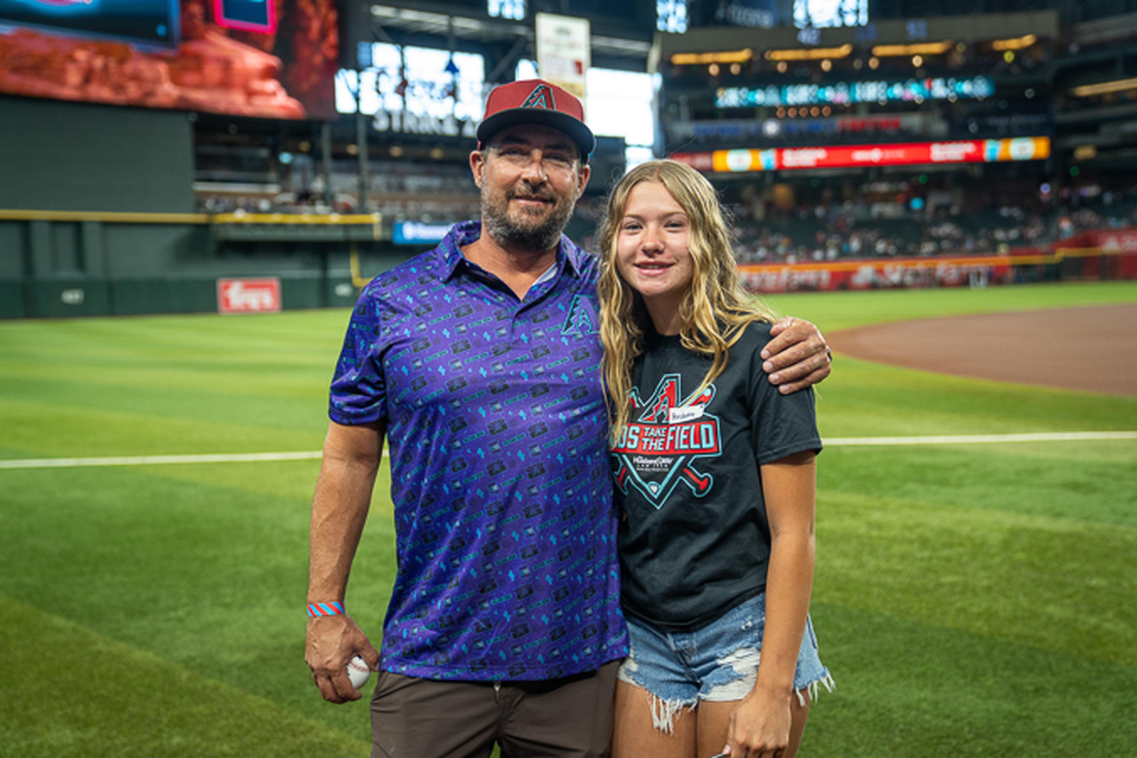 Father and daughter stand on Chase Field, framed by a lively stadium packed with fans in the background.