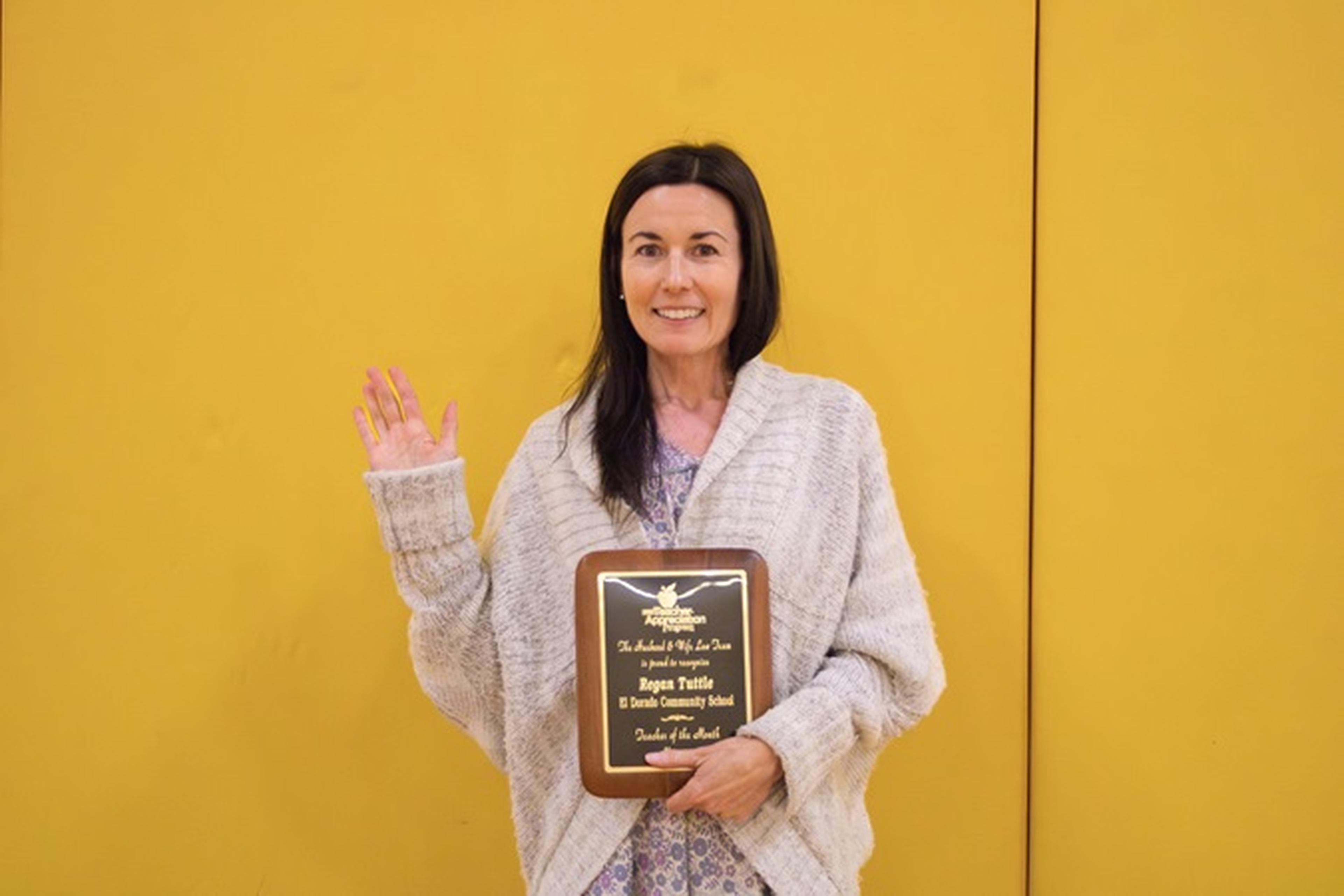 In a hallway decorated with vibrant art displays, Ms. Tuttle poses with her award plaque.