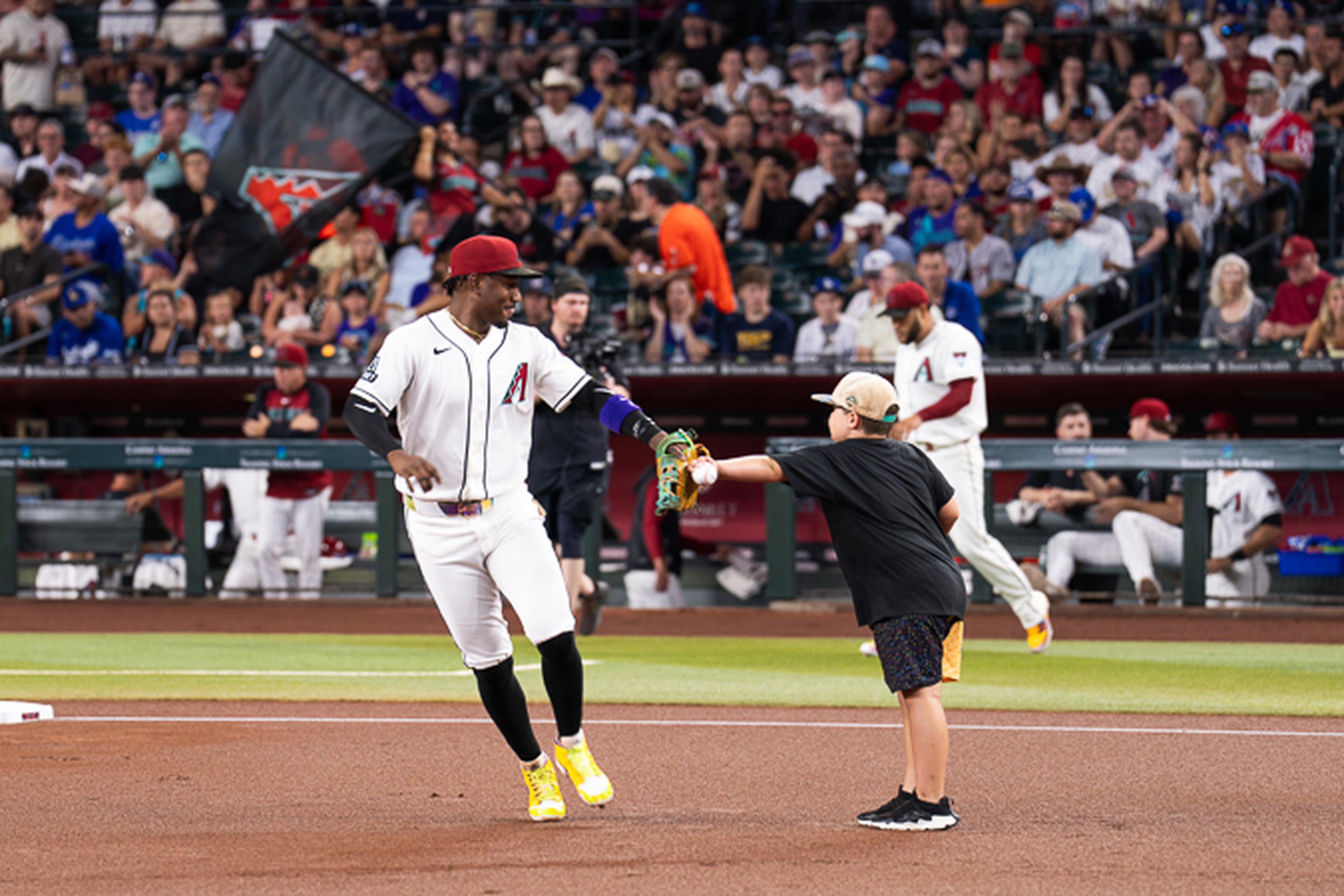 A young fan shares a memorable handshake with an Arizona Diamondbacks player on the field, creating a once-in-a-lifetime experience in front of a packed crowd at Chase Field.