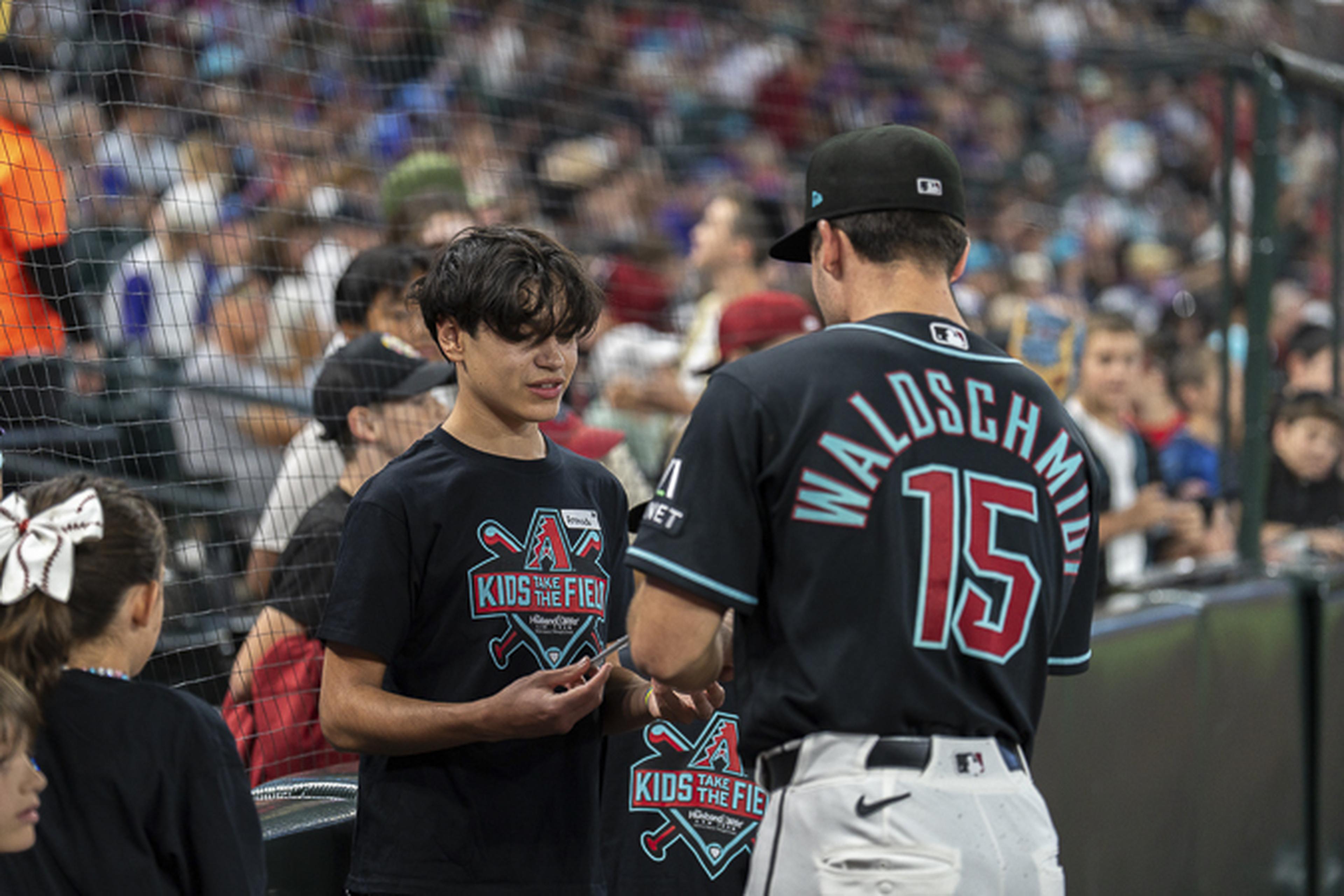 A Diamondbacks player wearing the “Waldschmidt 15” jersey connects with a young fan in a “Kids Take the Field” shirt at Chase Field.
