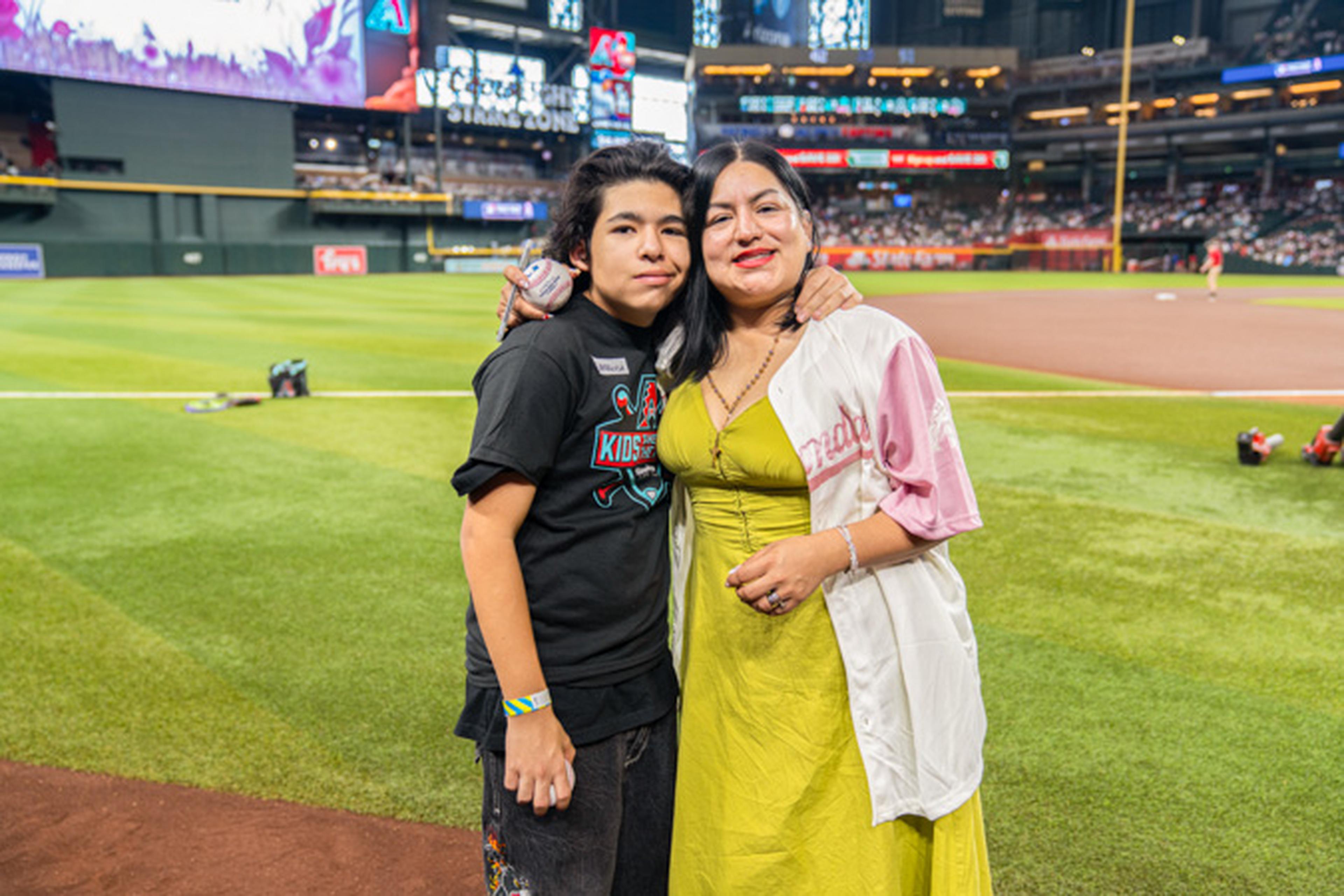 A mom and her child smile together on the field with the stadium stretching out behind them.
