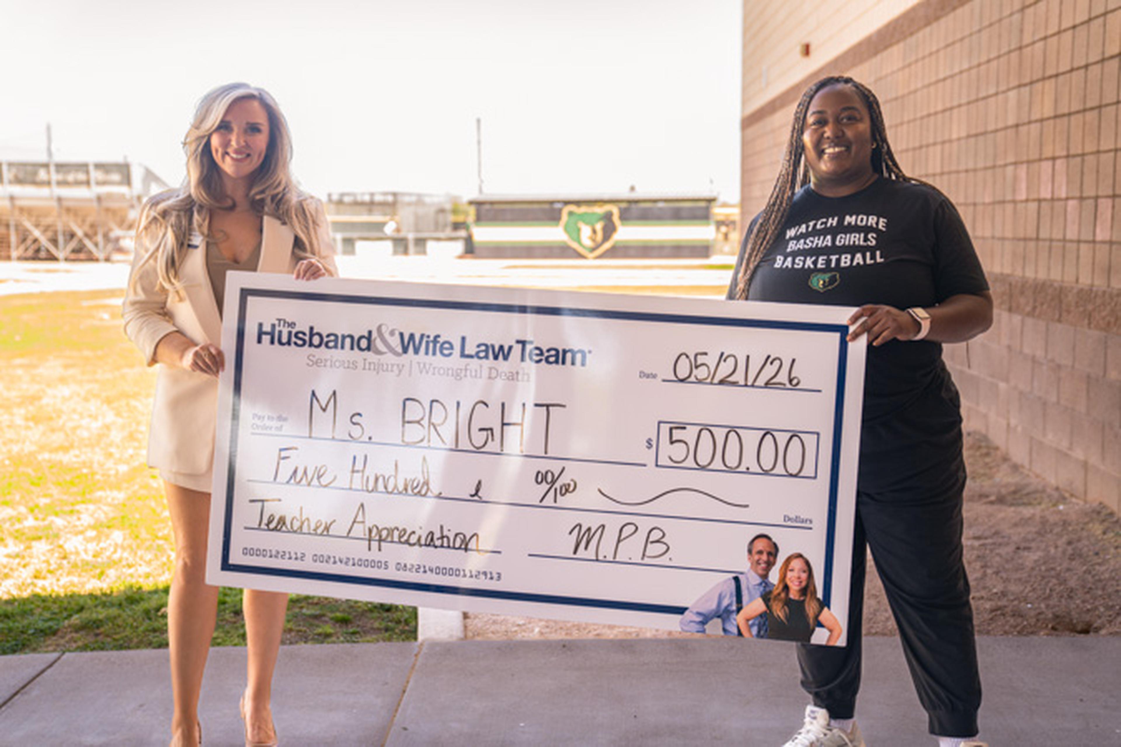 Jen proudly displays a large $500 ceremonial check awarded to Ms. Bright for Teacher Appreciation by The Husband & Wife Law Team.