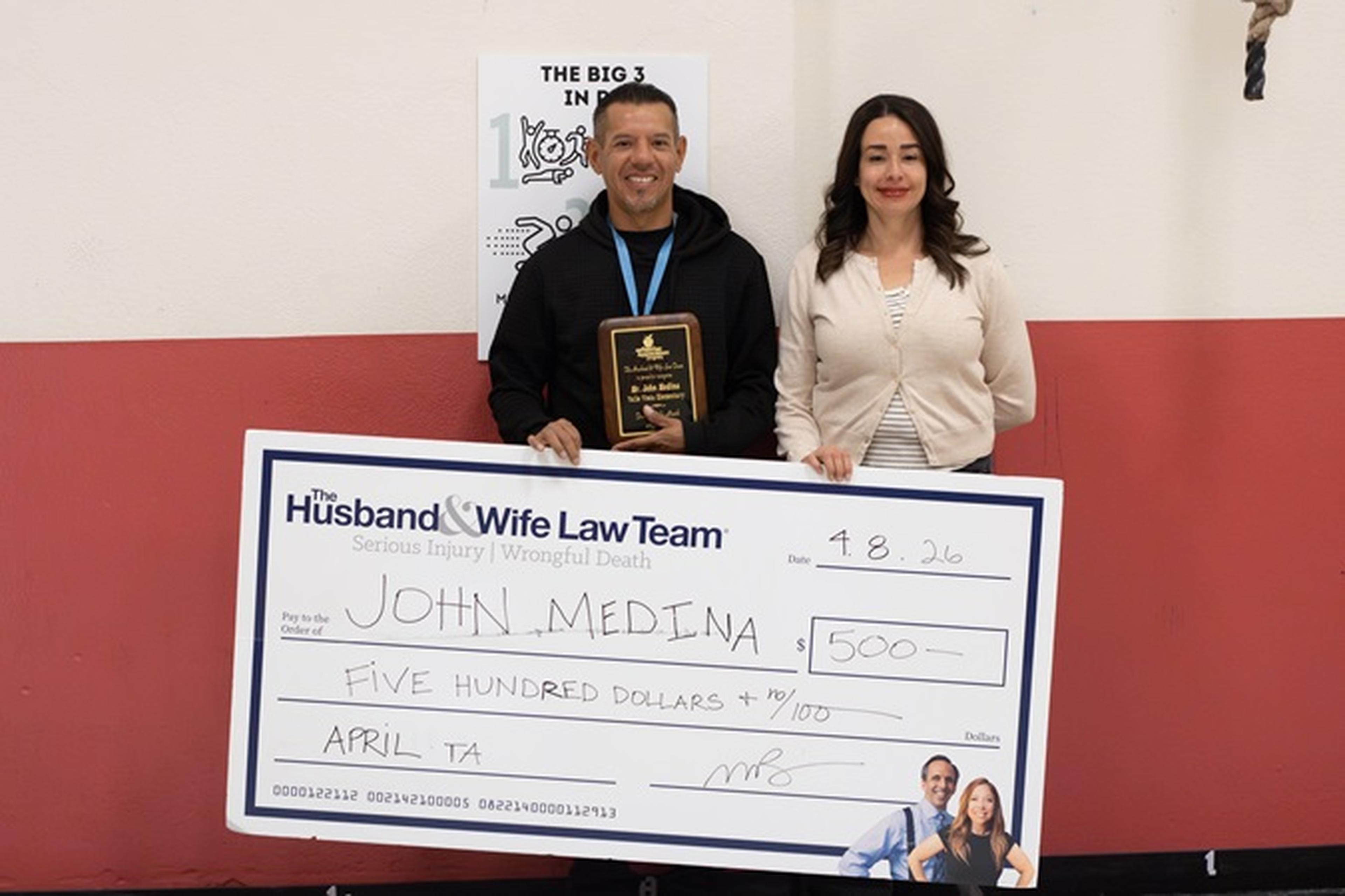 Mr. Medina and a faculty member stand with a $500 check from The Husband & Wife Law Team, as Mr. Medina holds his award plaque.